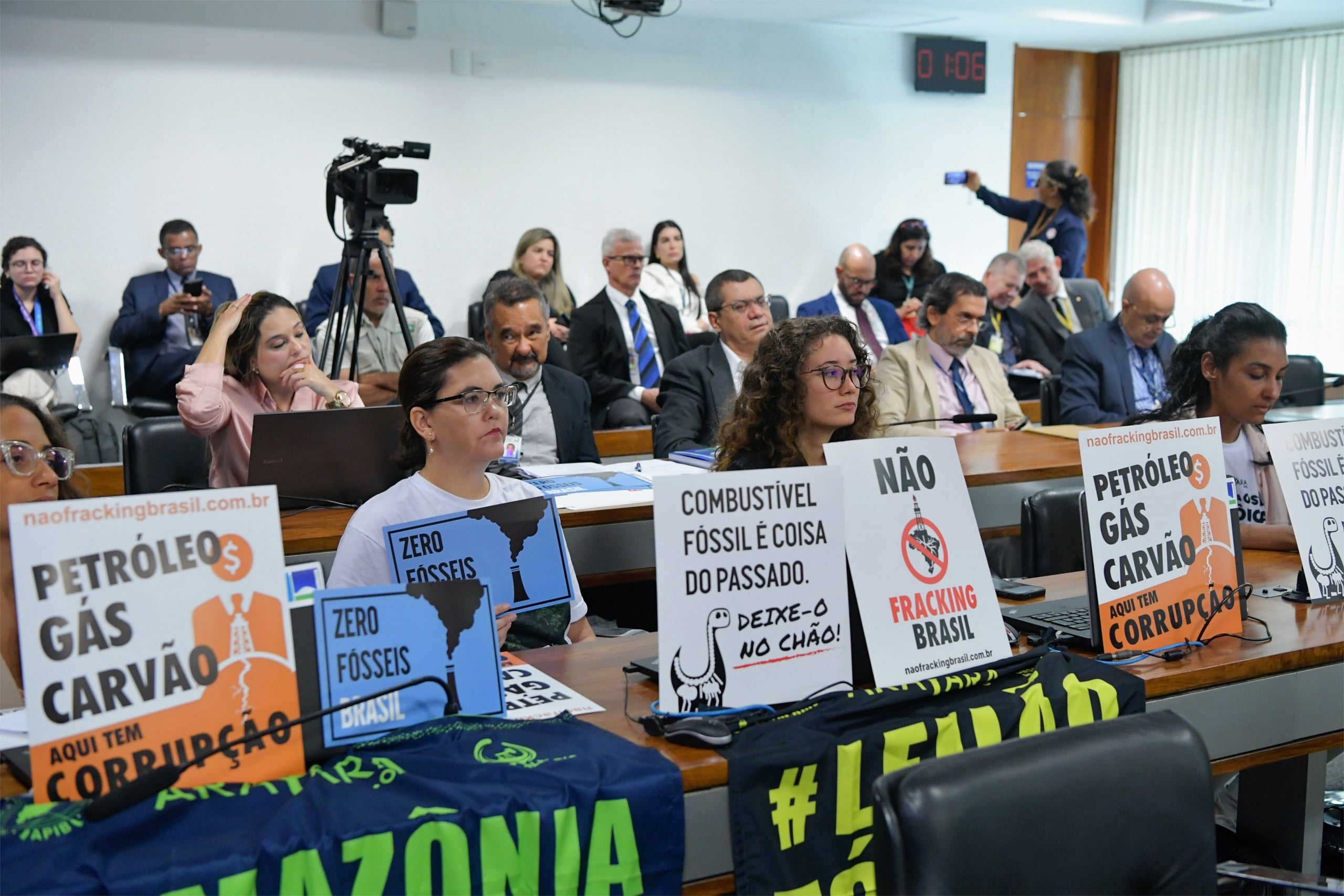 A meeting room filled with attendees holding signs opposing fossil fuels and fracking