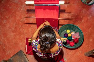 A woman weaves threads on a loom