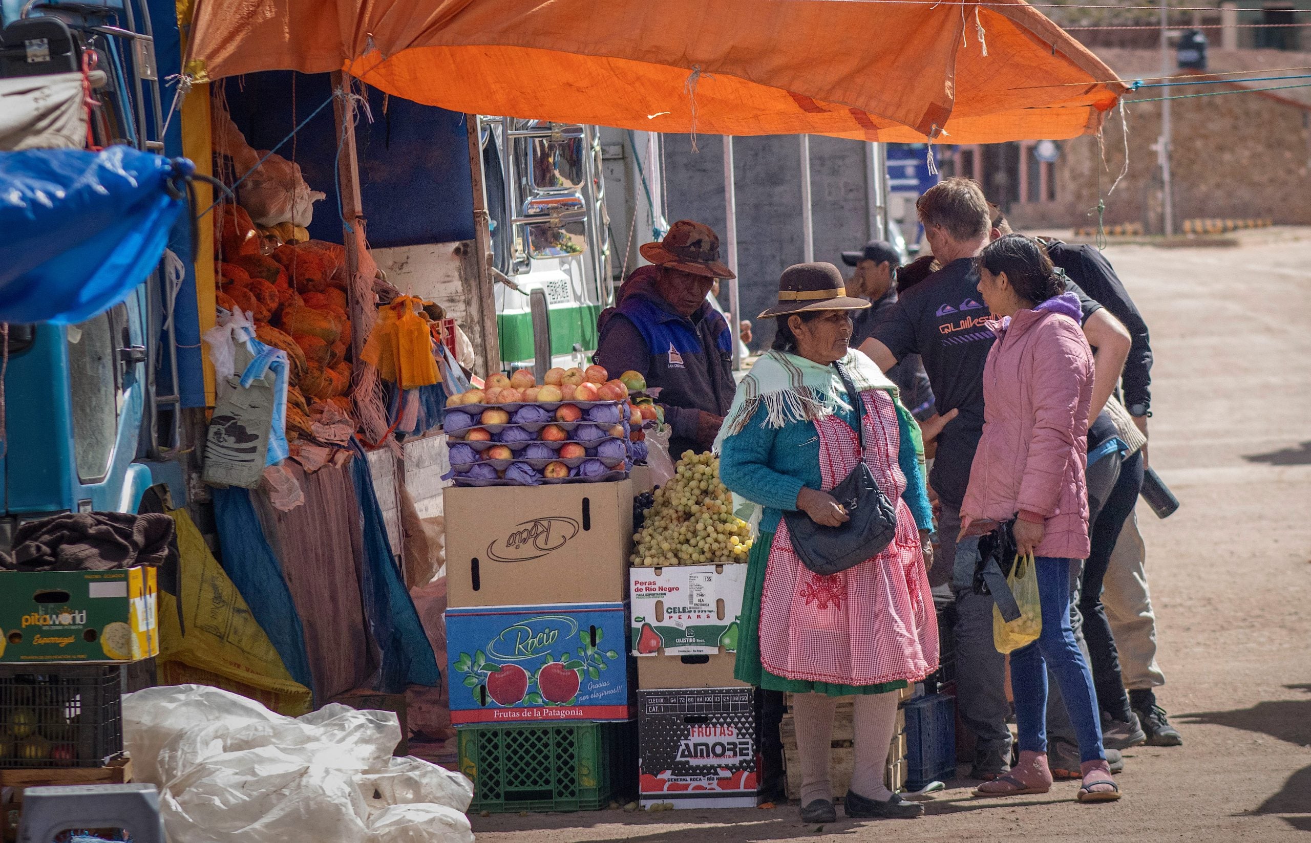 People stand and shop for fruits and vegetables at an outdoor market stall