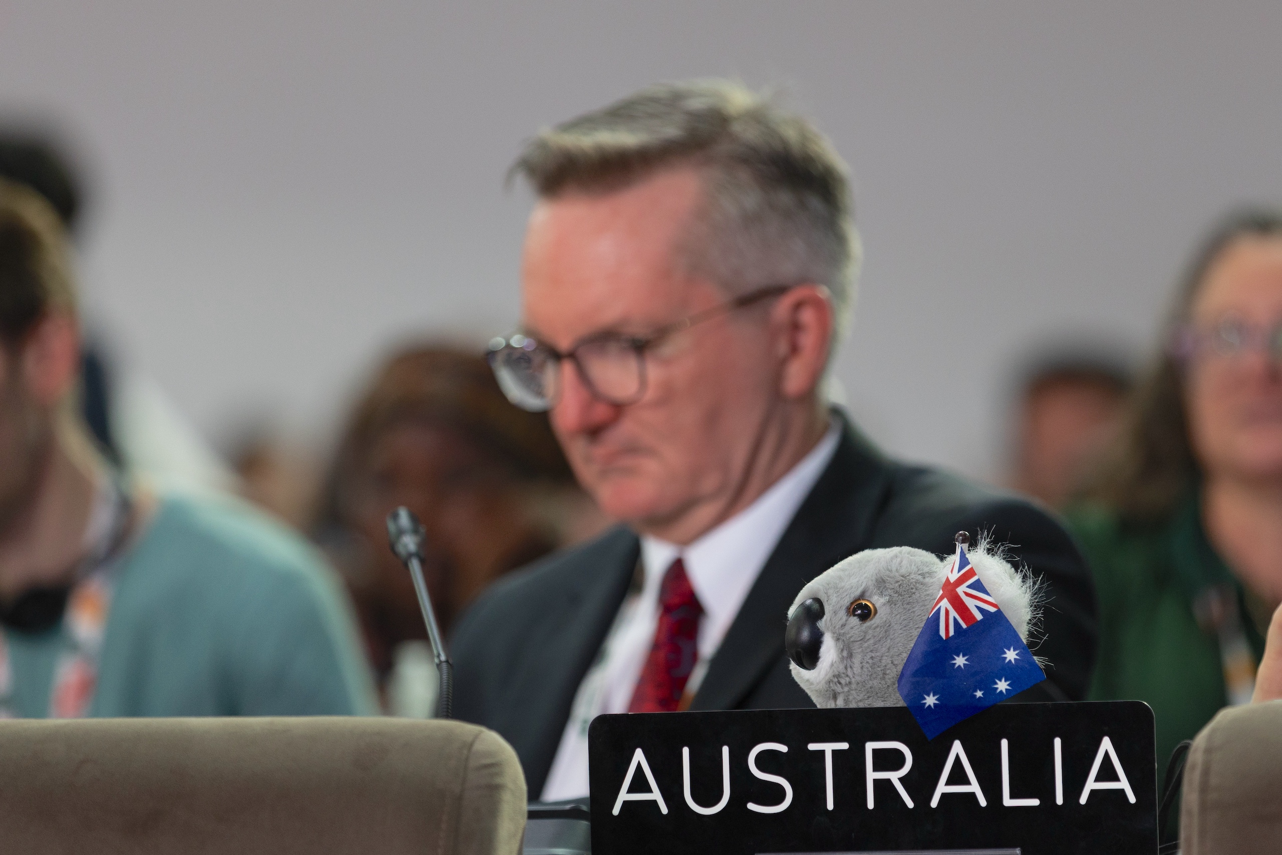A koala plush toy with an Australian flag sits on a table labeled "Australia," with minister for climate change and energy of Australia in the background at COP30