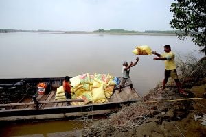 Two men transferring yellow sacks of commodities from the riverbank to a boat