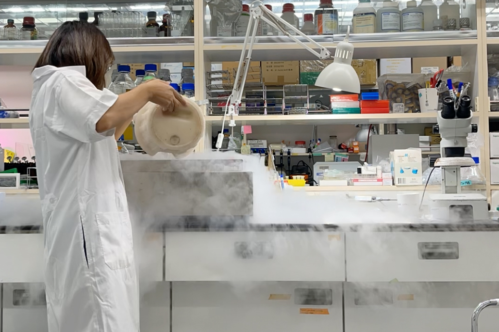 person in lab coat pouring liquid nitrogen into vesssel