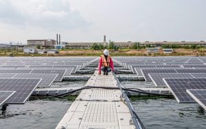 A worker inspects solar panels on a floating platform in a body of water