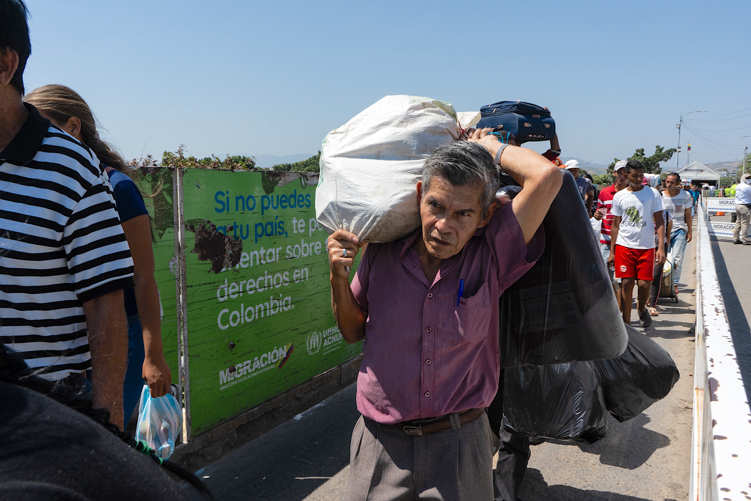 A man carries a heavy bag on his shoulder while walking among a crowd 