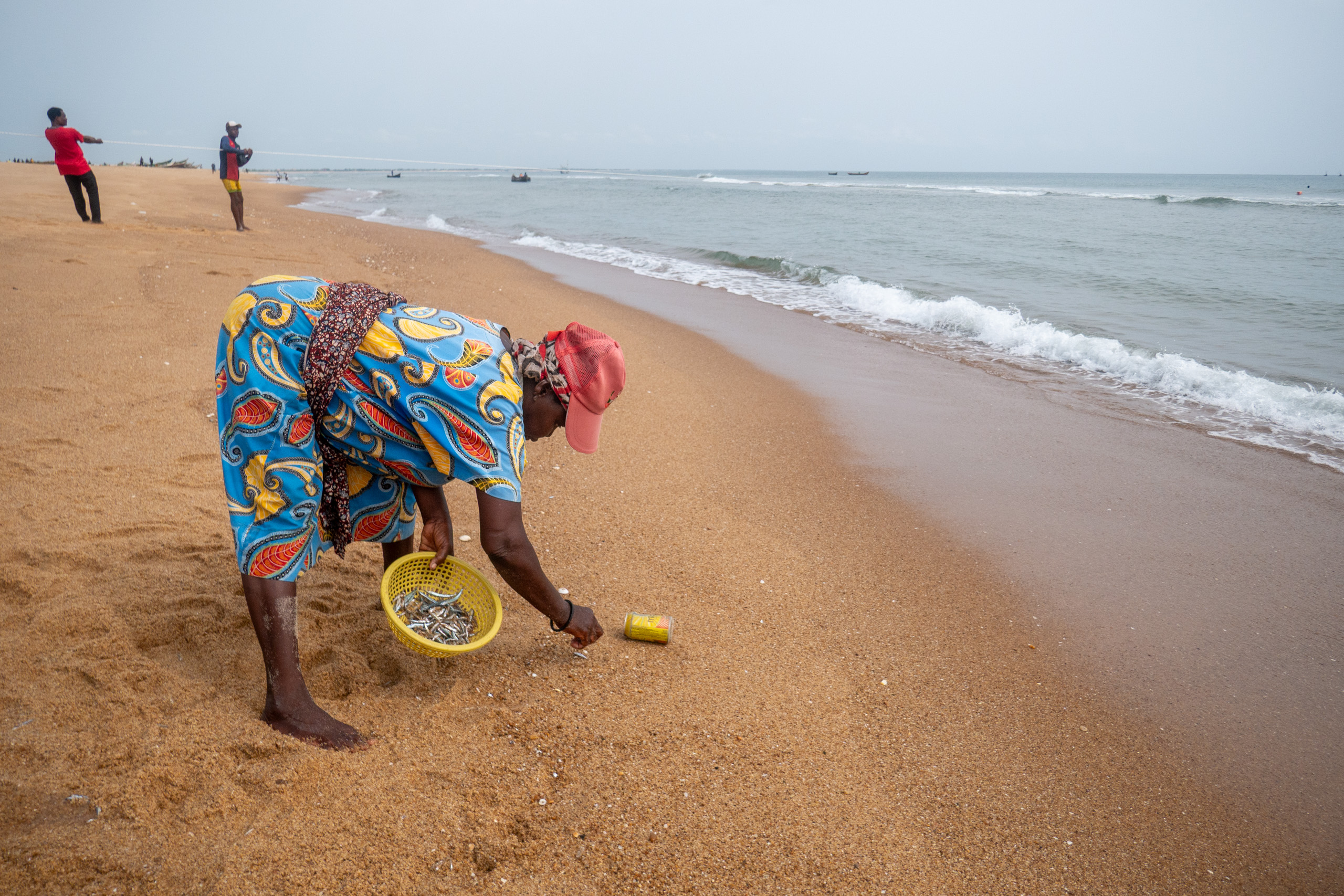 bent over woman holding small basin on beach