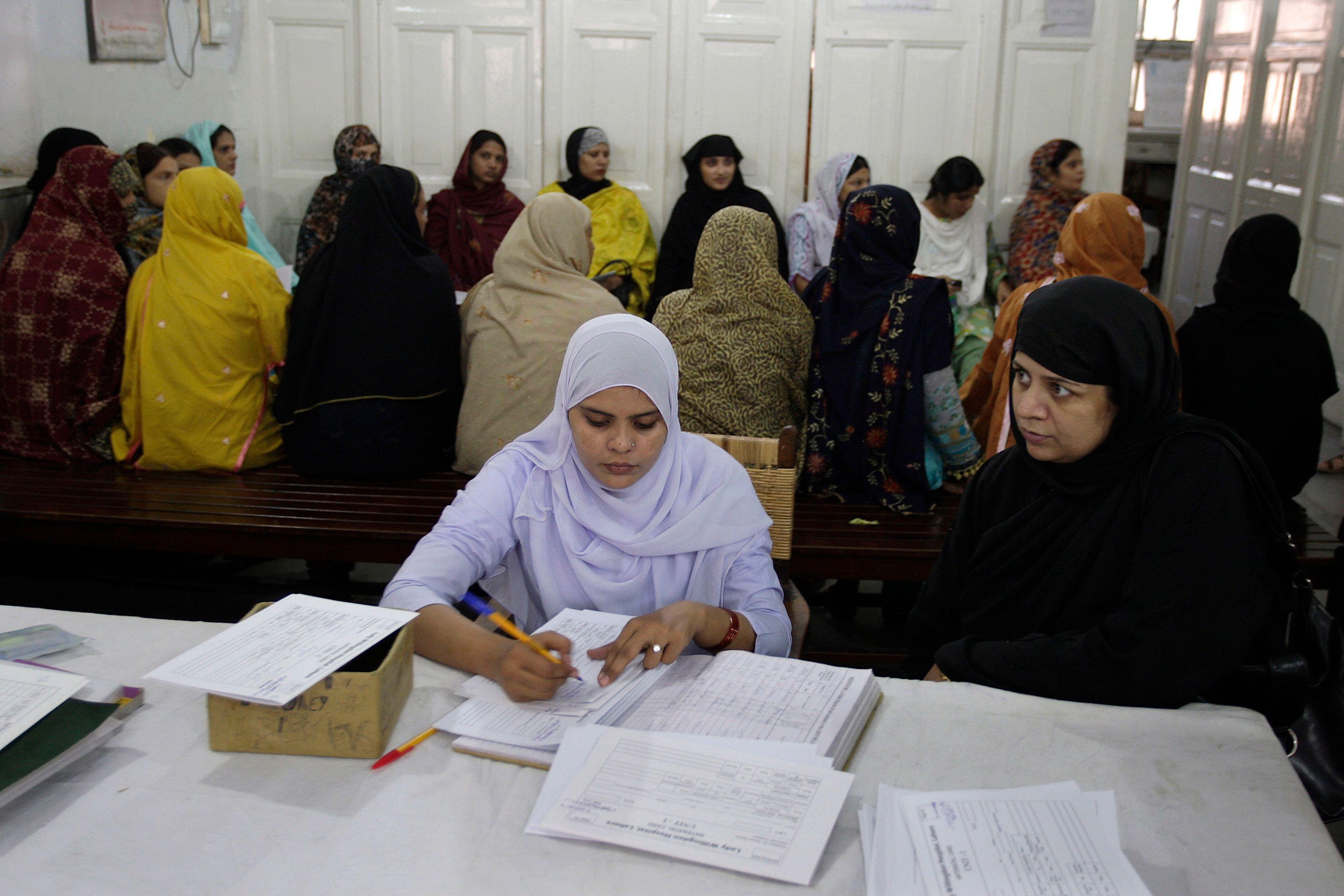 A group of women in colorful shawls sit on benches in a waiting area in a hospital