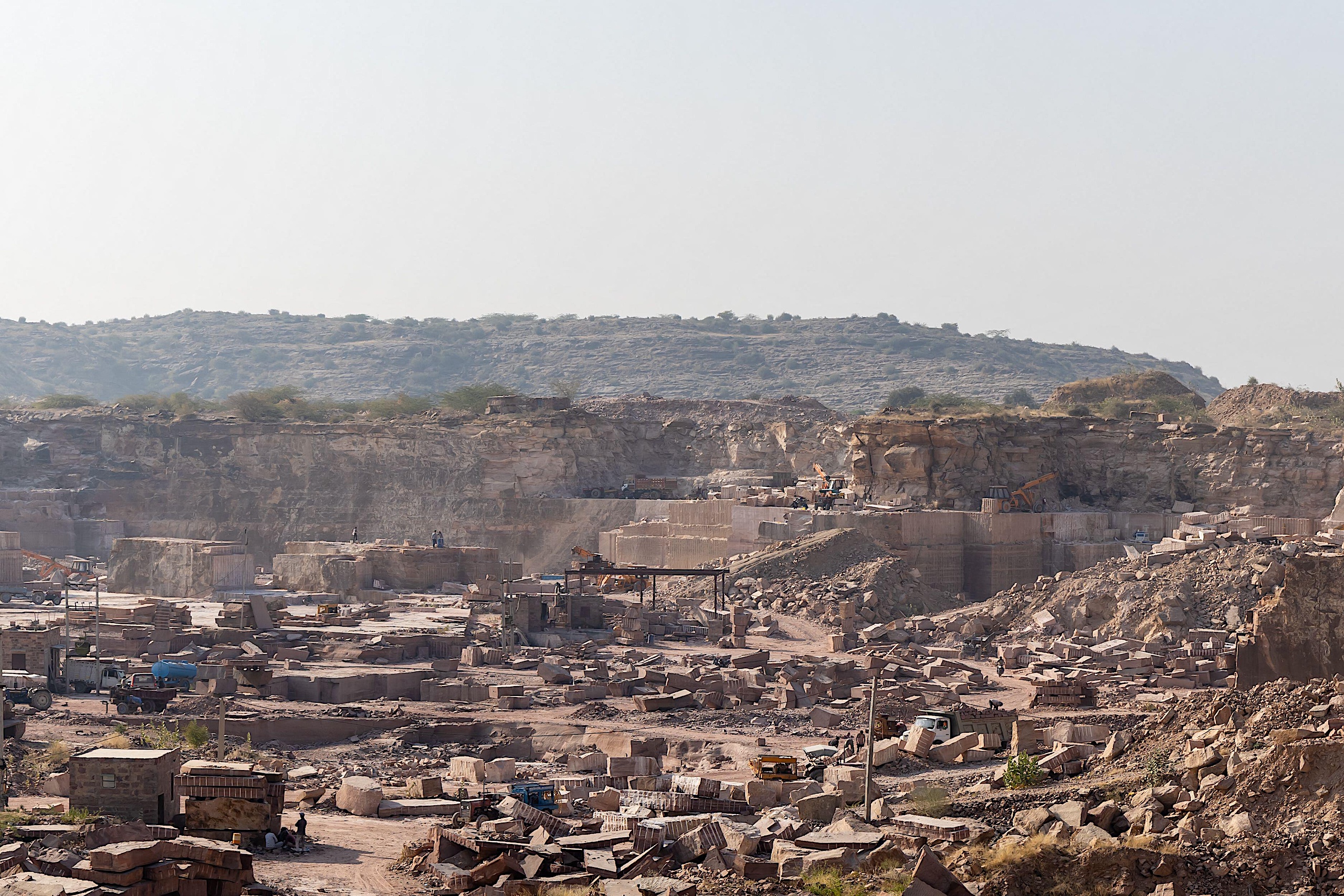 A vast stone quarry under a hazy sky, with layered rock formations and scattered masonry