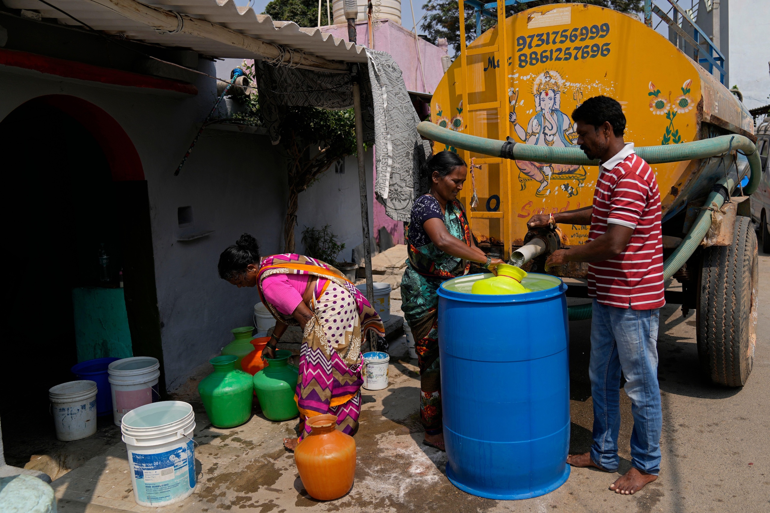 People fill colorful containers from a yellow water tanker on a street