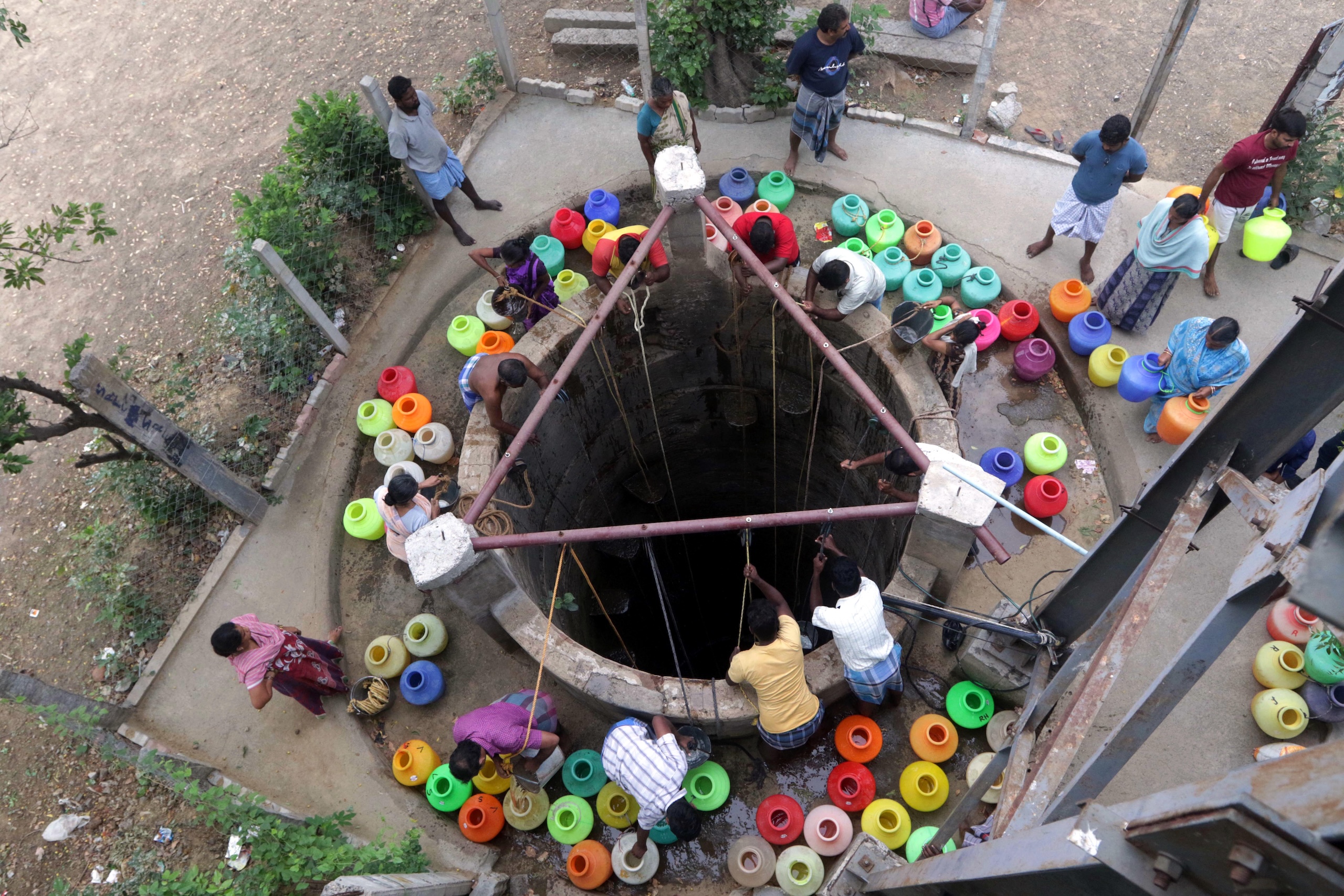 People gather around a well with colorful plastic containers to collect water