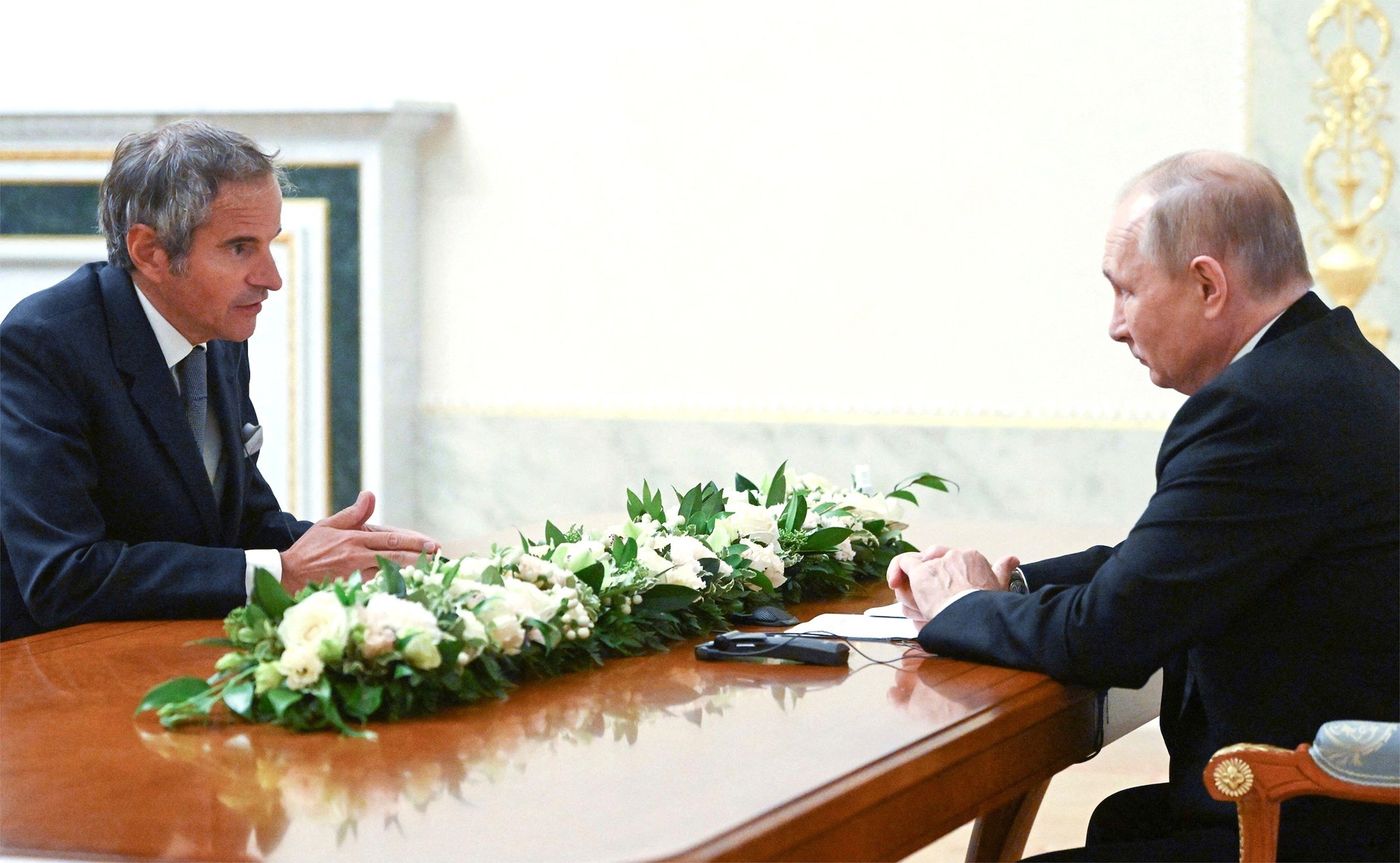 Two men in formal suits sit across a table, conveying a serious discussion