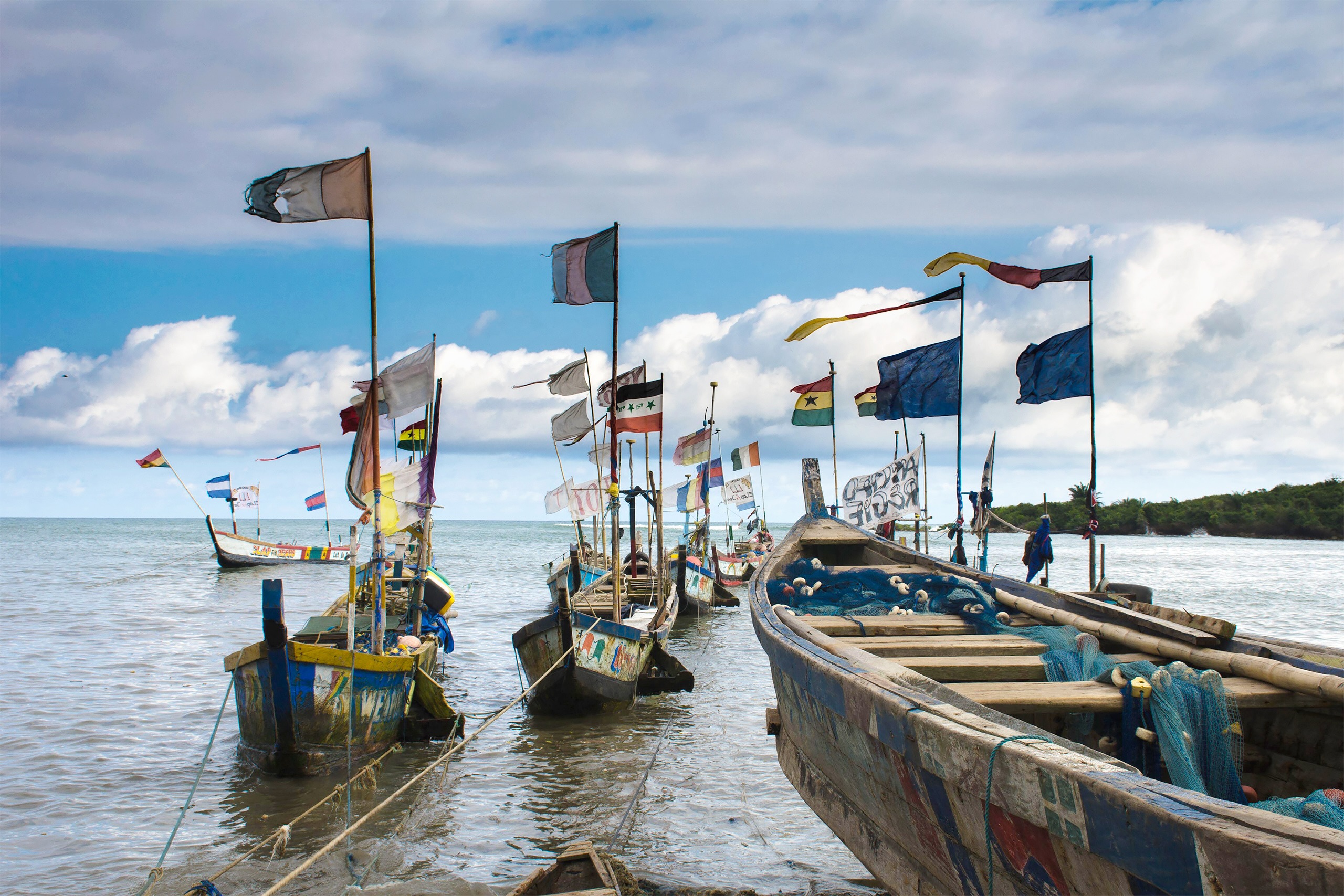 Wooden fishing boats with colorful flags are docked by the shore 