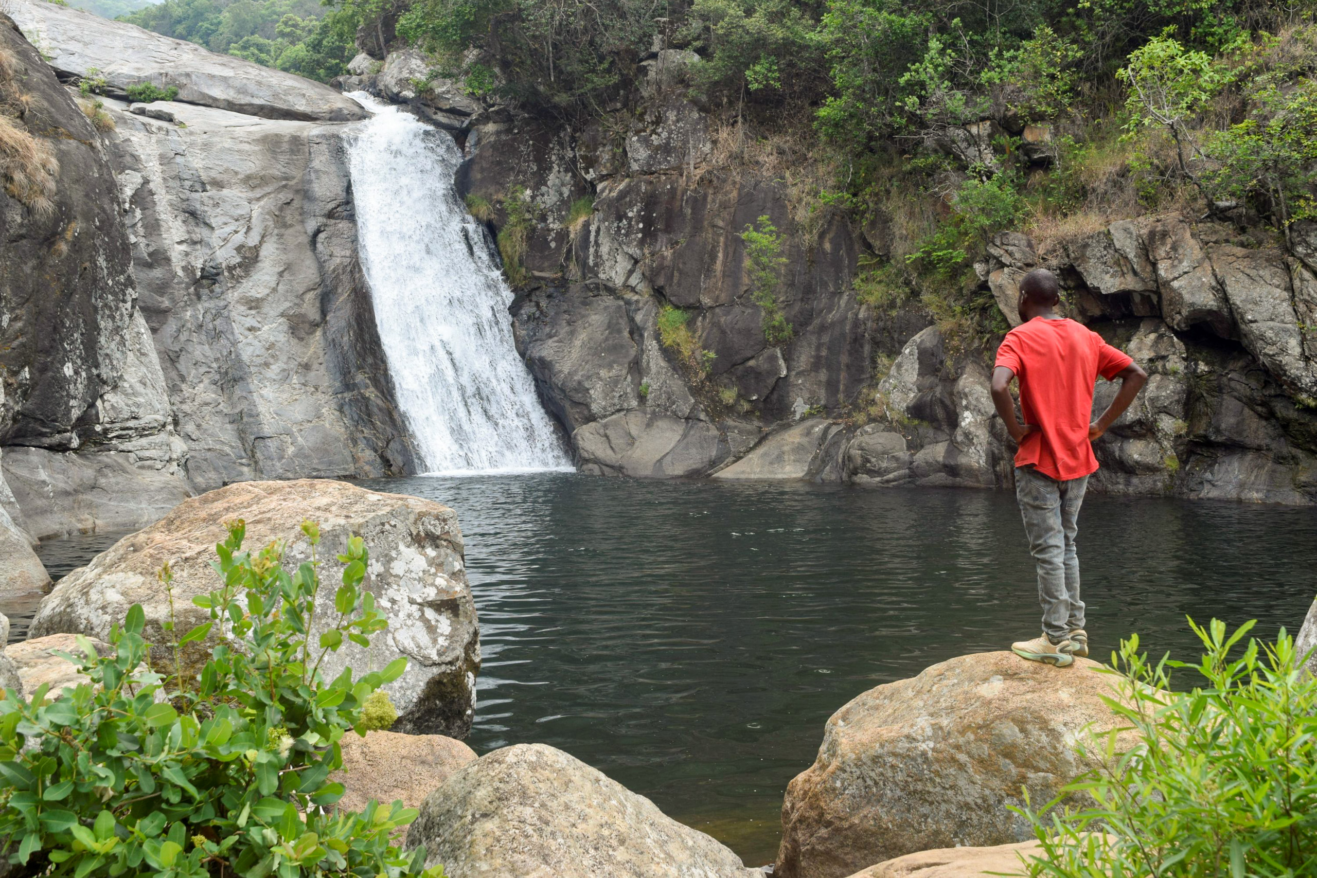 man standing near pool beneath waterfall