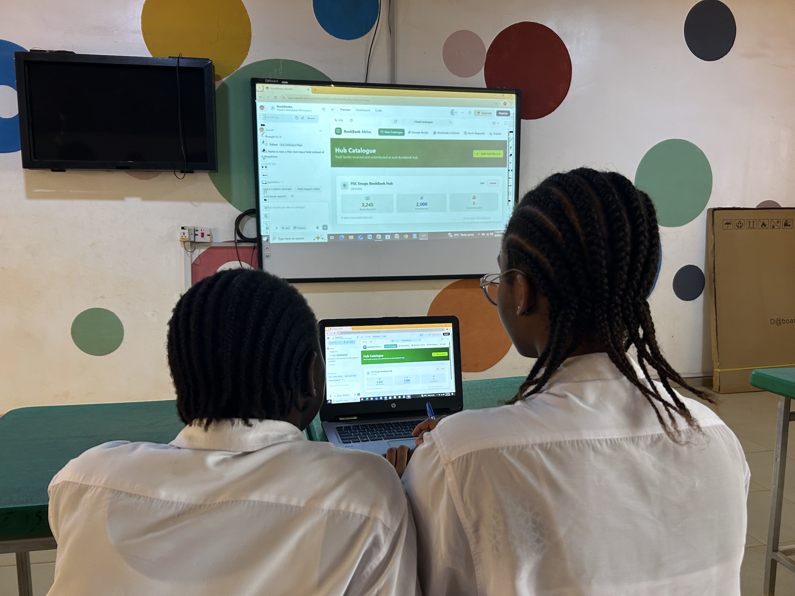 Two students in uniforms work at a laptop, looking on a screen