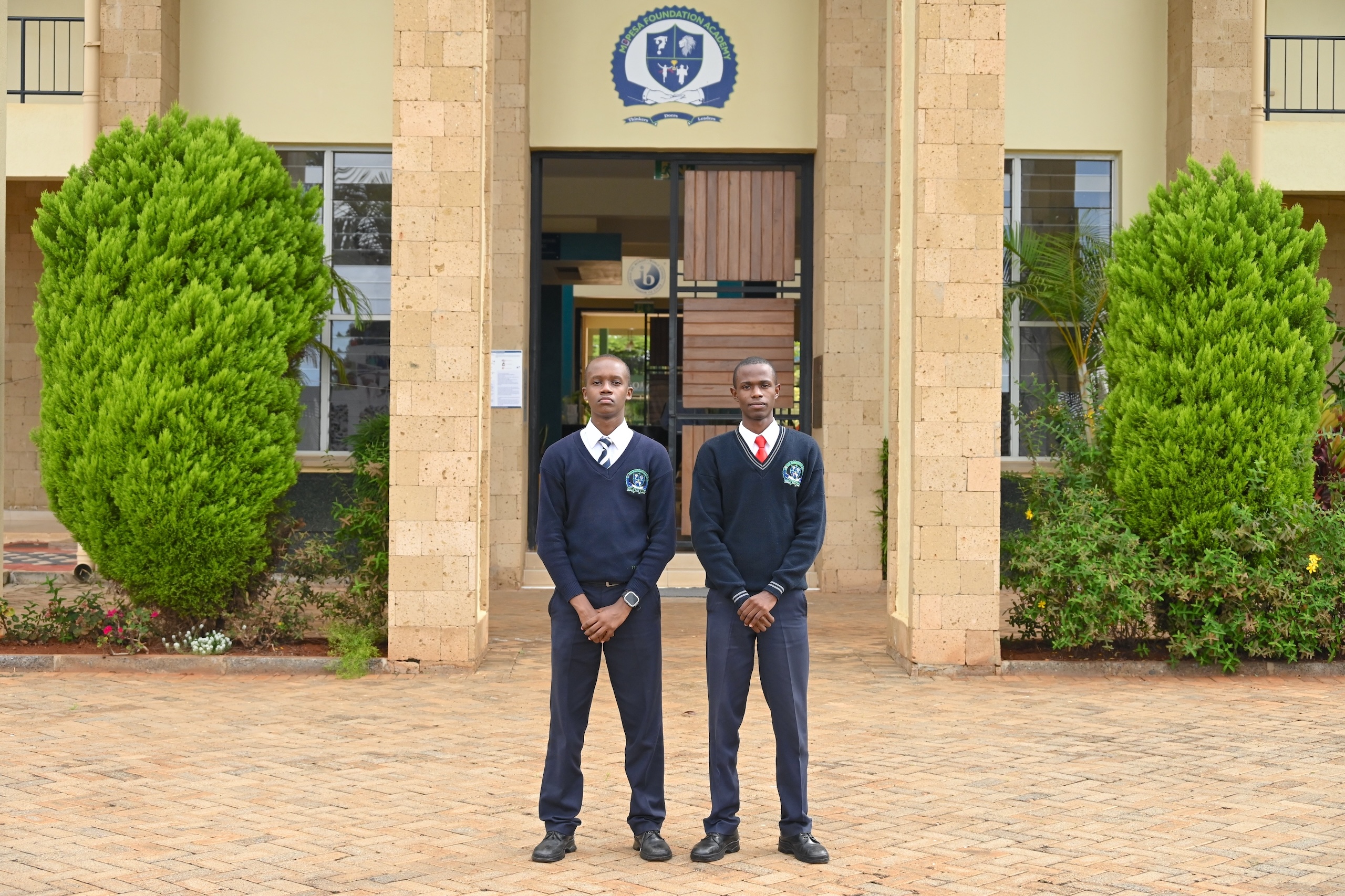 Two students in uniforms pose in front of an academic building