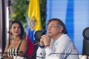 Gustavo Petro sentado en una mesa con un micrófono, con una bandera de Colombia detrás