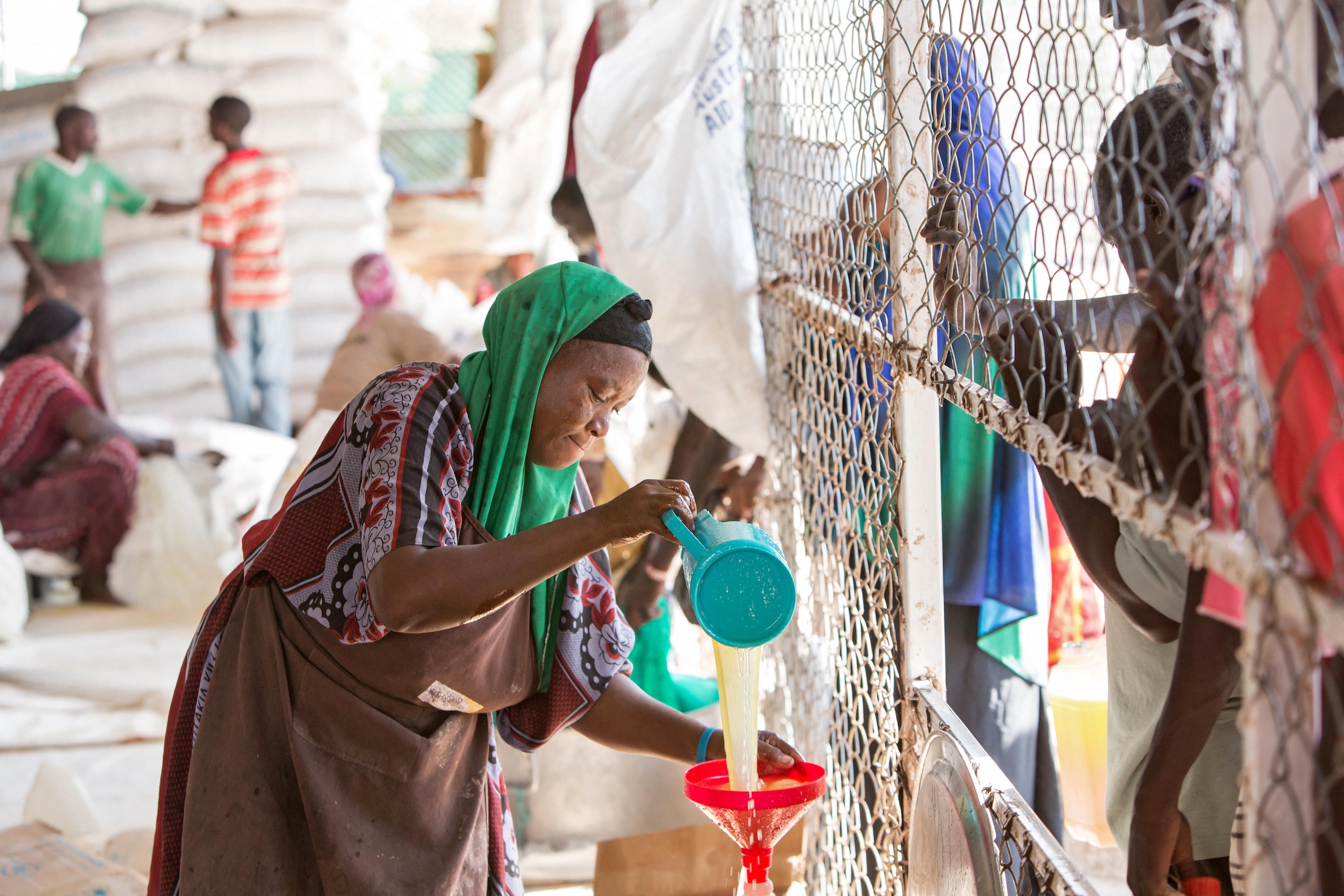 A woman in a colorful headscarf pours liquid through a funnel at a distribution point