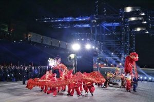 Una actuación de la danza del dragón por la noche, con luces brillantes y una gran grúa portuaria al fondo