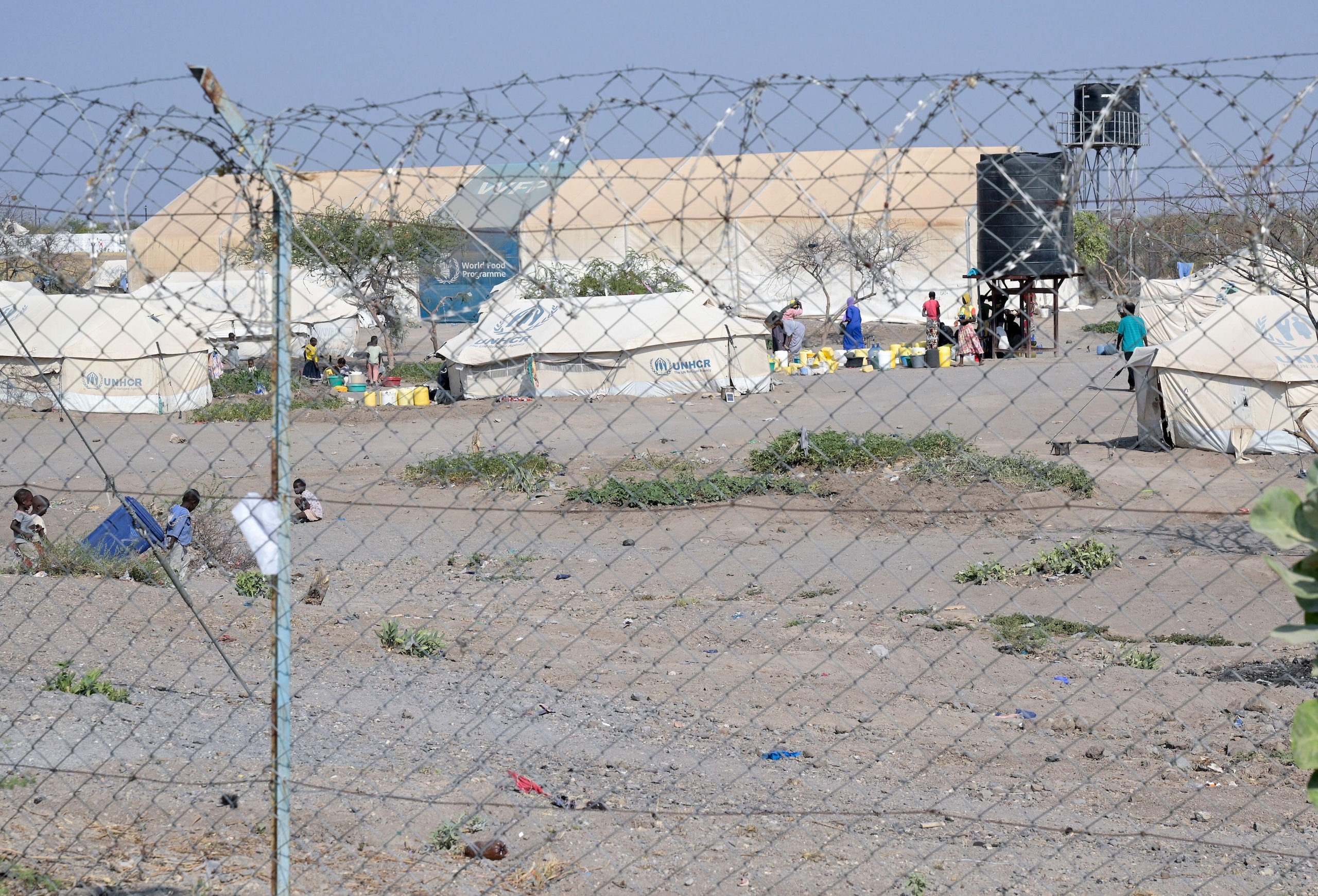 A refugee camp with UNHCR tents sits beyond a barbed wire fence