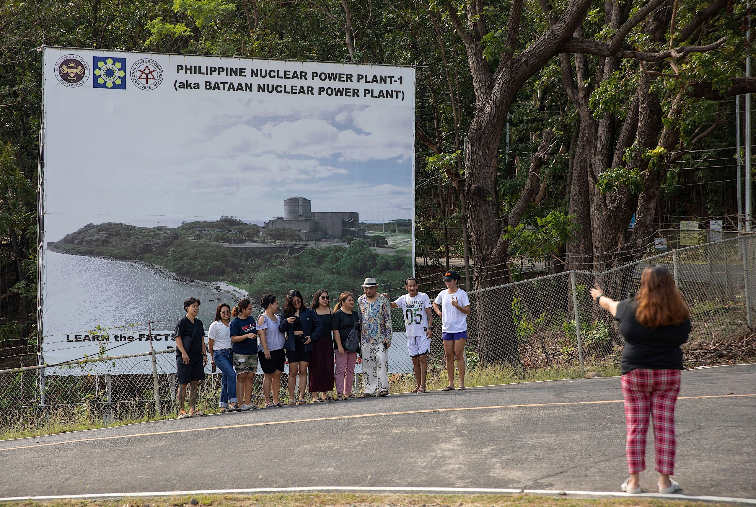 A group of people pose for a photo in front of a large sign for the Philippine Bataan Nuclear Power