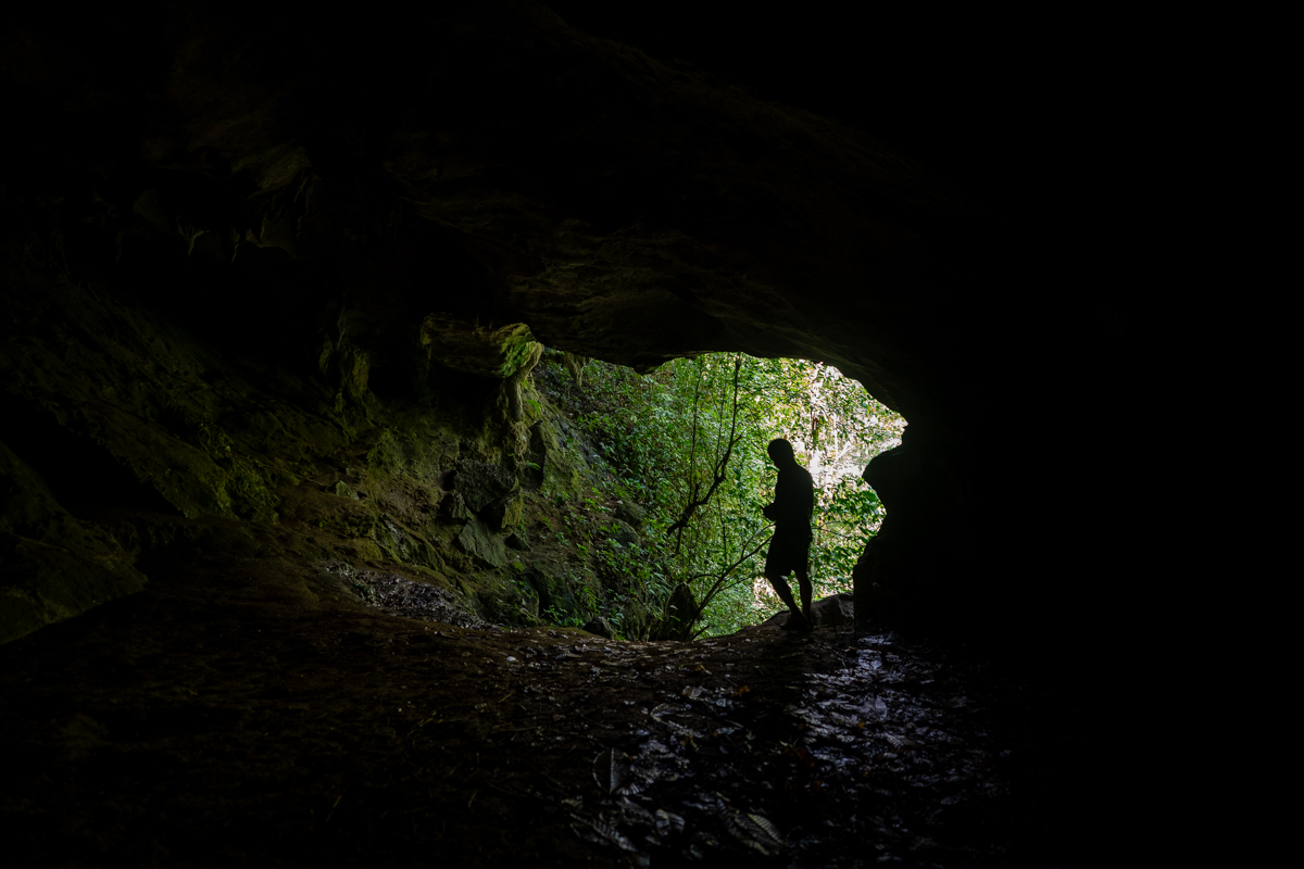 A person stands at the mouth of a dark cave, surrounded by rocky walls