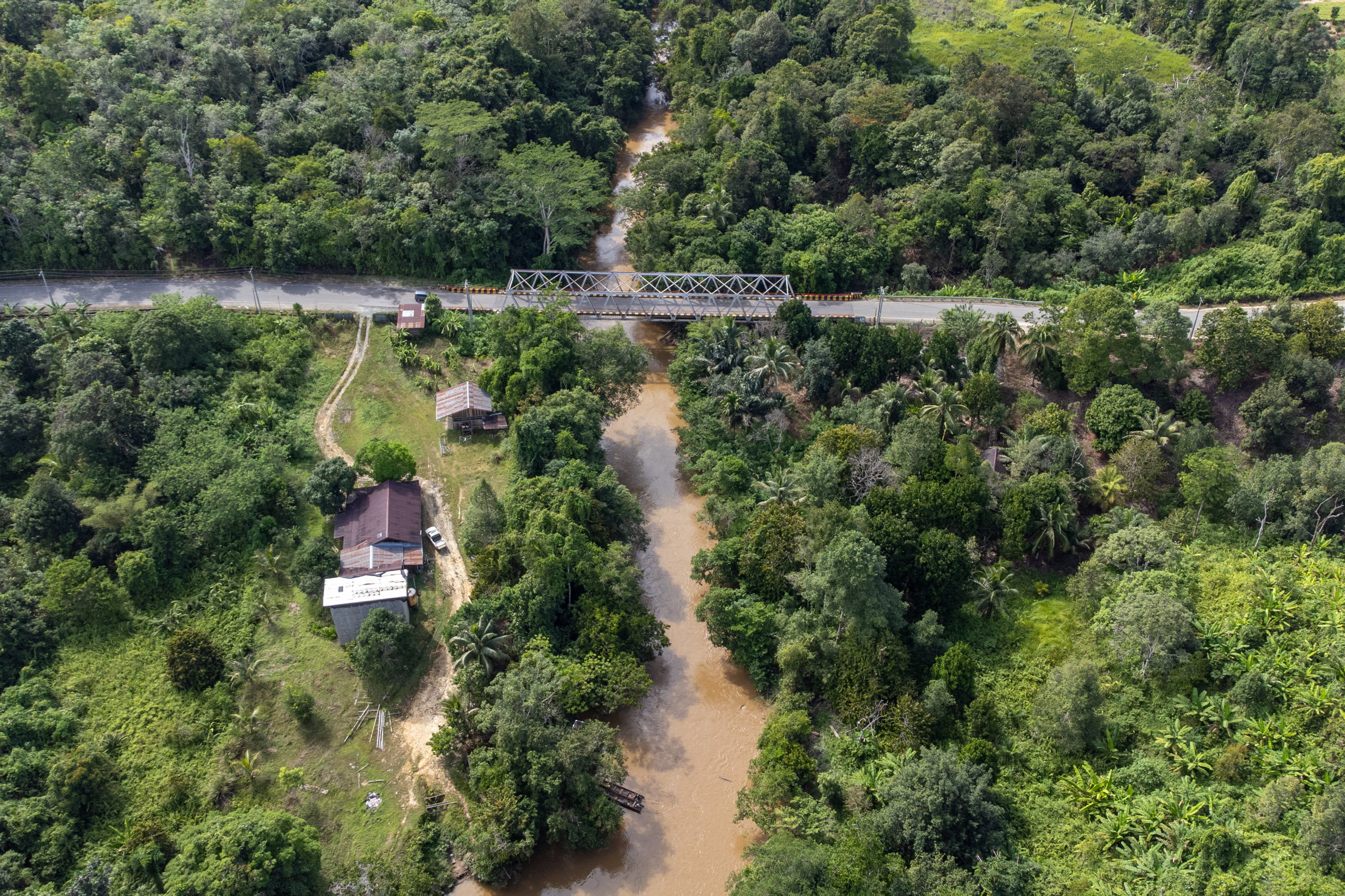 Aerial view of a winding river with a bridge crossing over it, surrounding by forest 