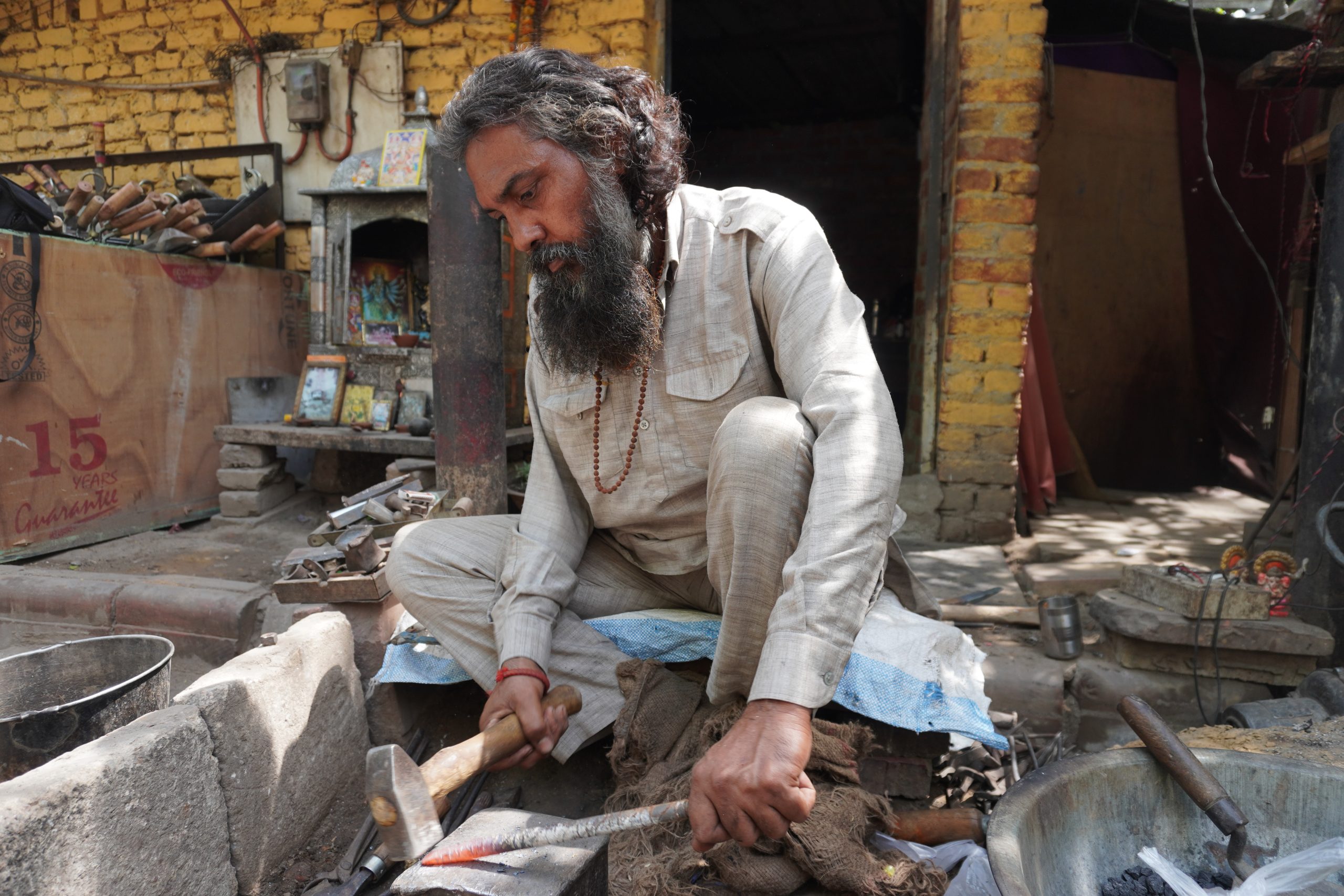 <p>Blacksmith Vikram Mani shapes heated iron into tools on a pavement outside his two-room house in Delhi, a space that doubles as both workshop and residence for his family (Image: Safina Nabi)</p>