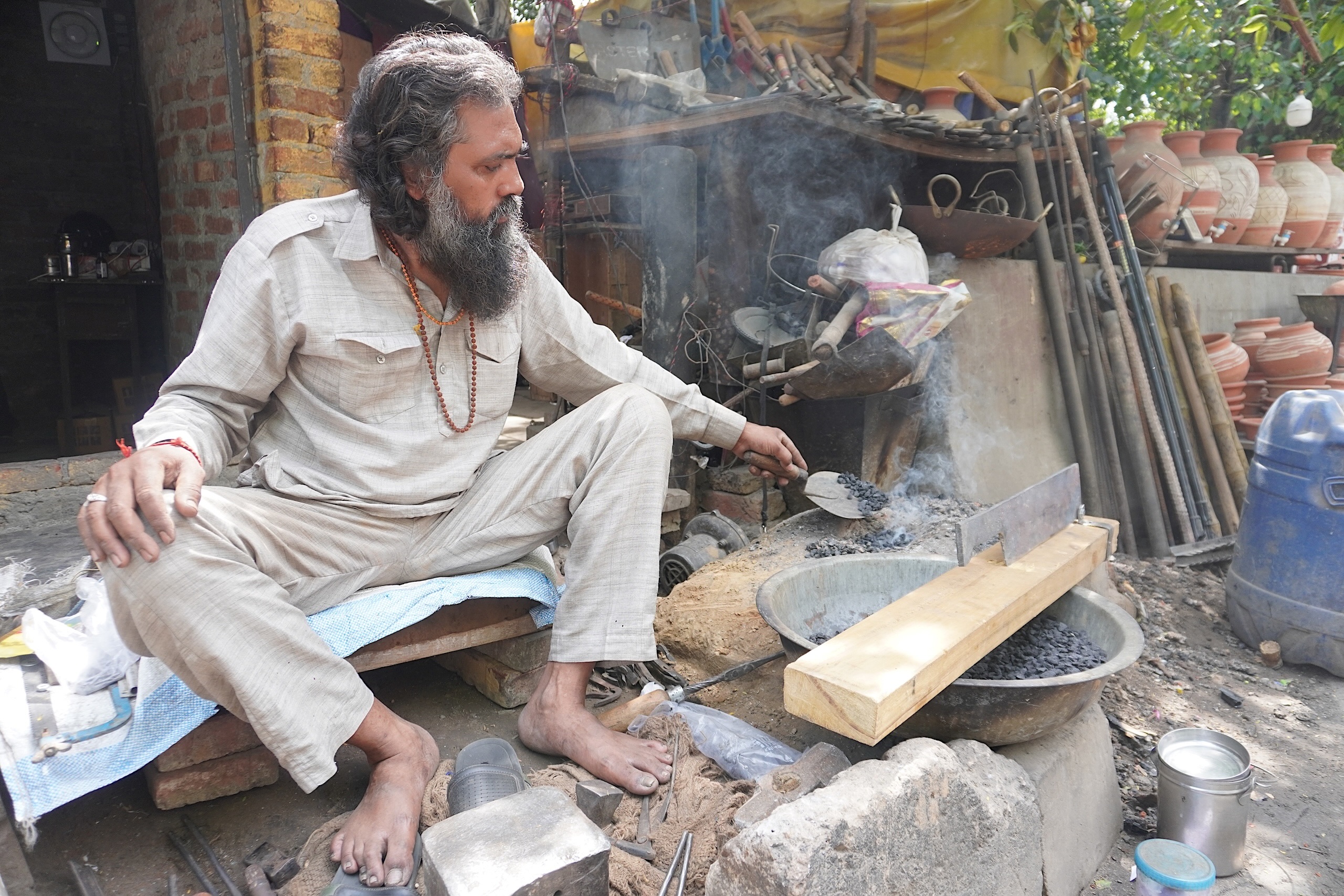 A man seated on the ground with a pot placed next to him
