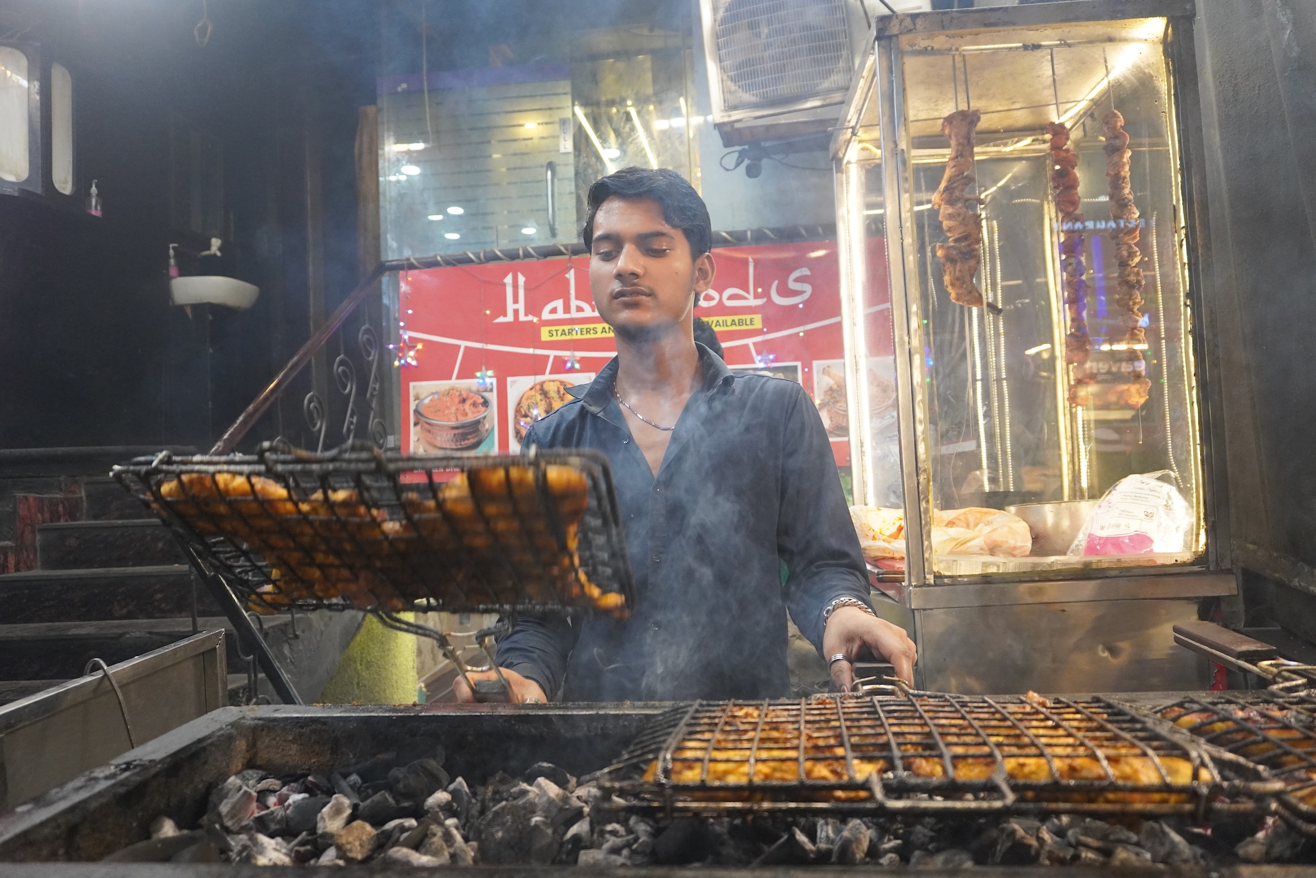 A man grilling food at a food stall over a coal fired tandoor