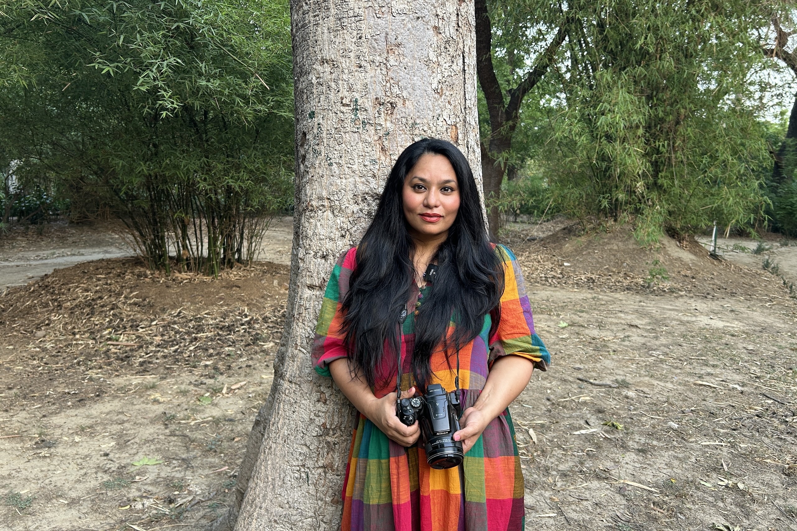 A woman in a vibrant dress stands beside a large tree