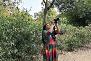 A woman with a camera aims at a tree in an outdoor area
