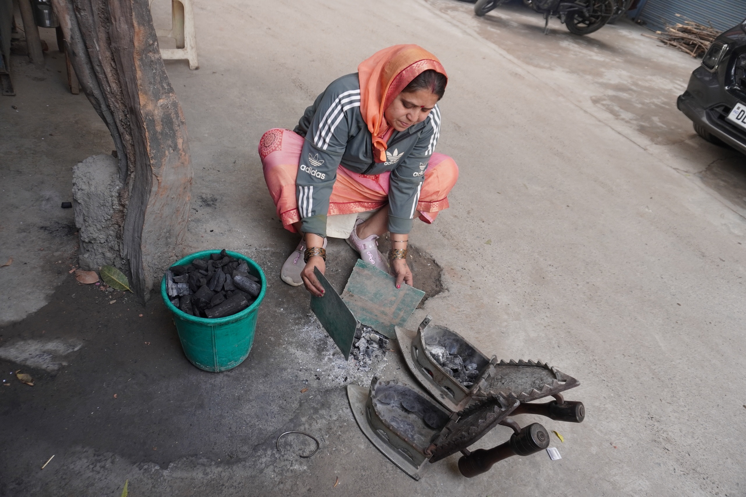 a woman opens a metal almirah and pulls out two heavy irons and a bucket of charcoal