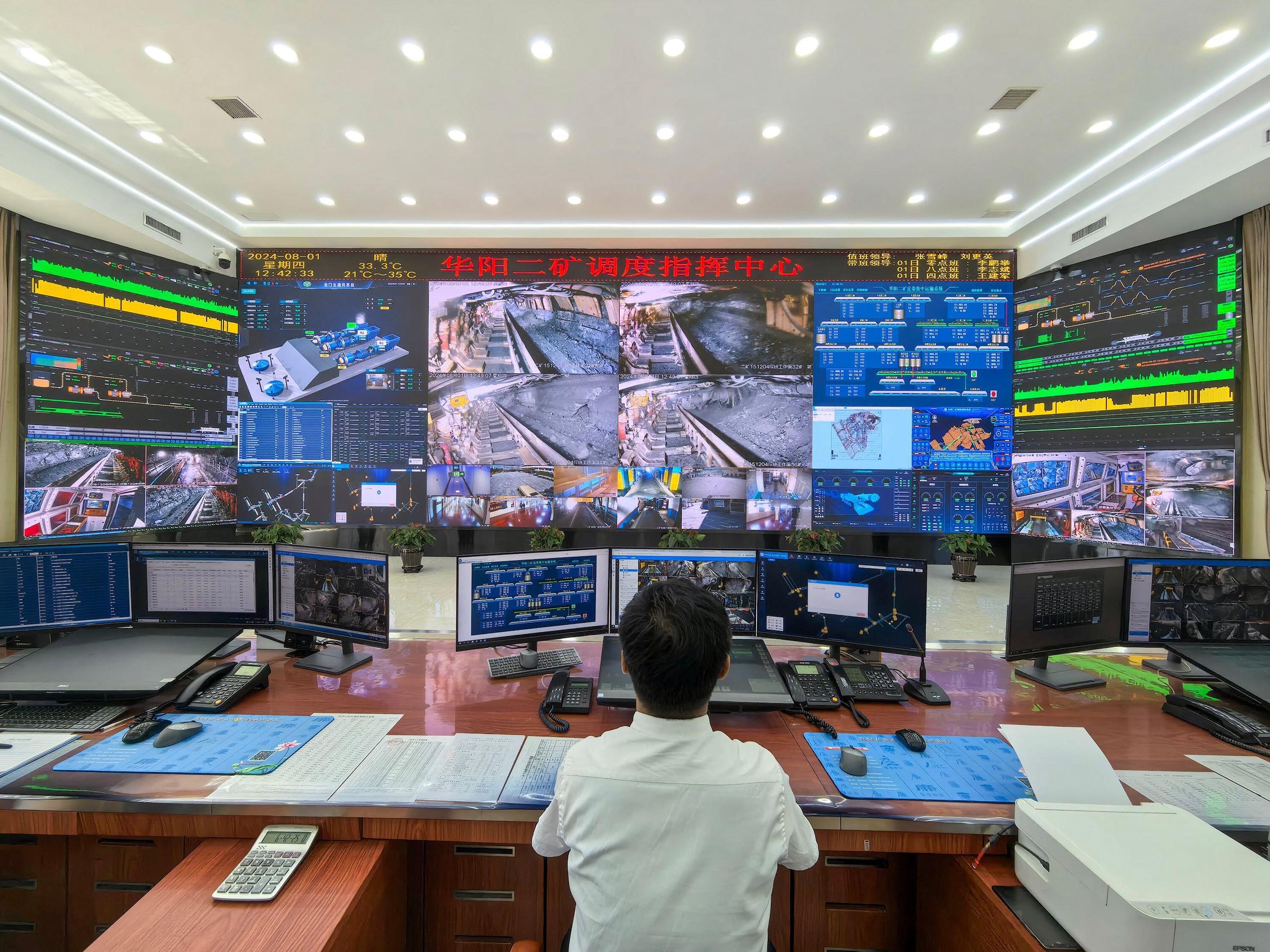 A man sits in front of a large screen displaying multiple monitors on coal mine activies