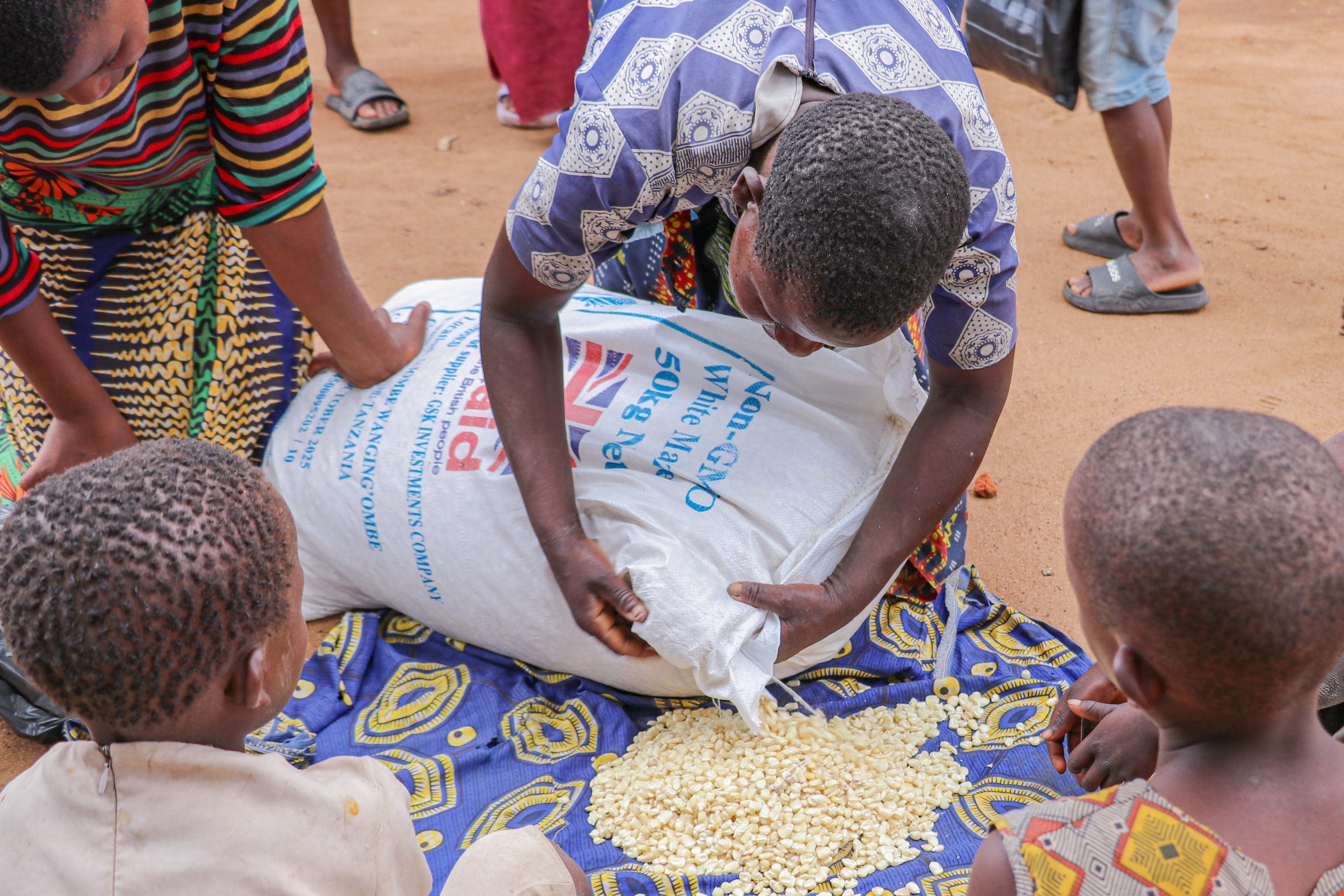 A woman patches a torn bag of maize, with children around her