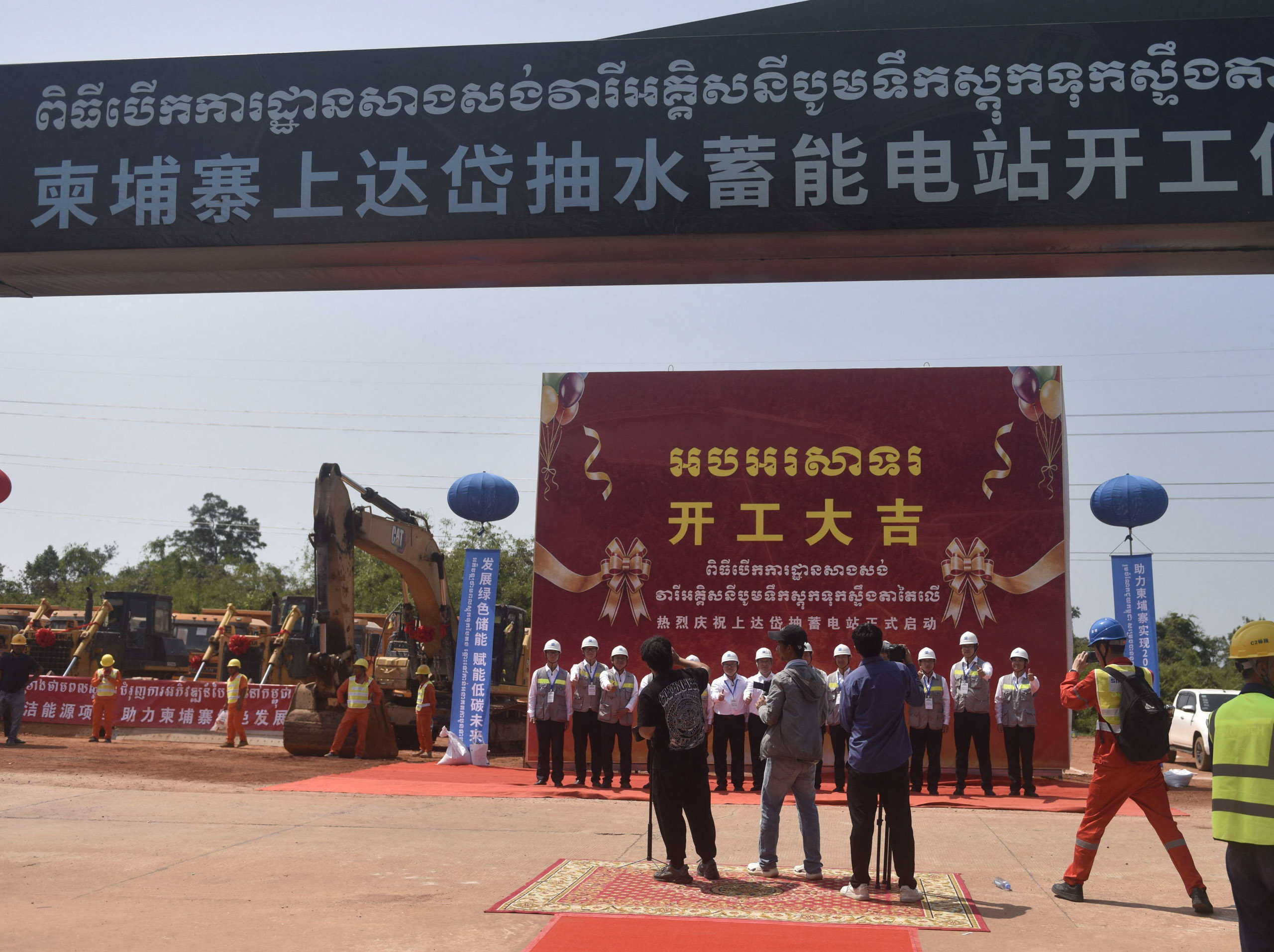 photographers facing people lined up beneath banner
