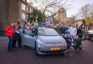 A group of people smiling and posing beside a car on a brick road