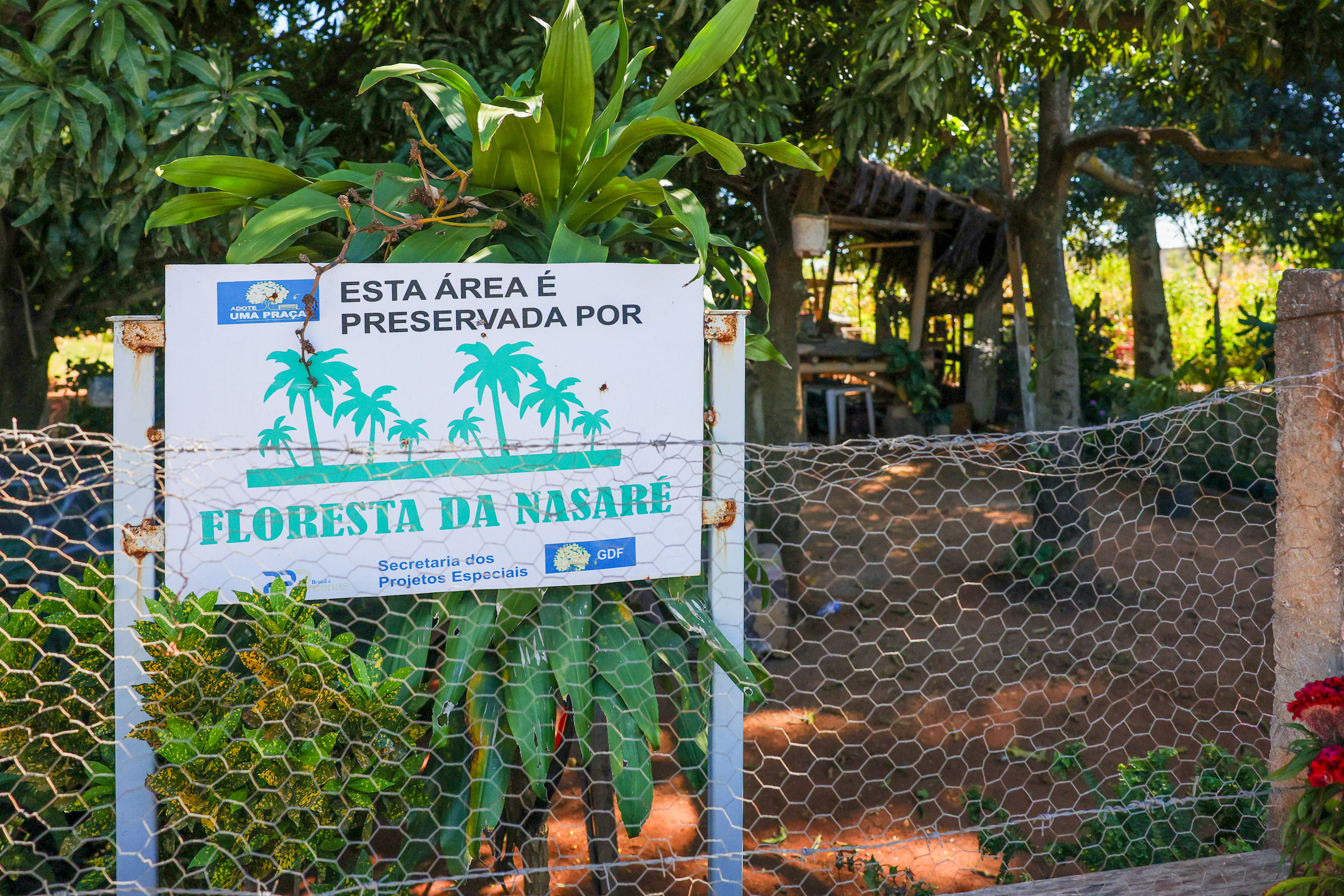Sign in Portuguese on a fenced area with trees and plants
