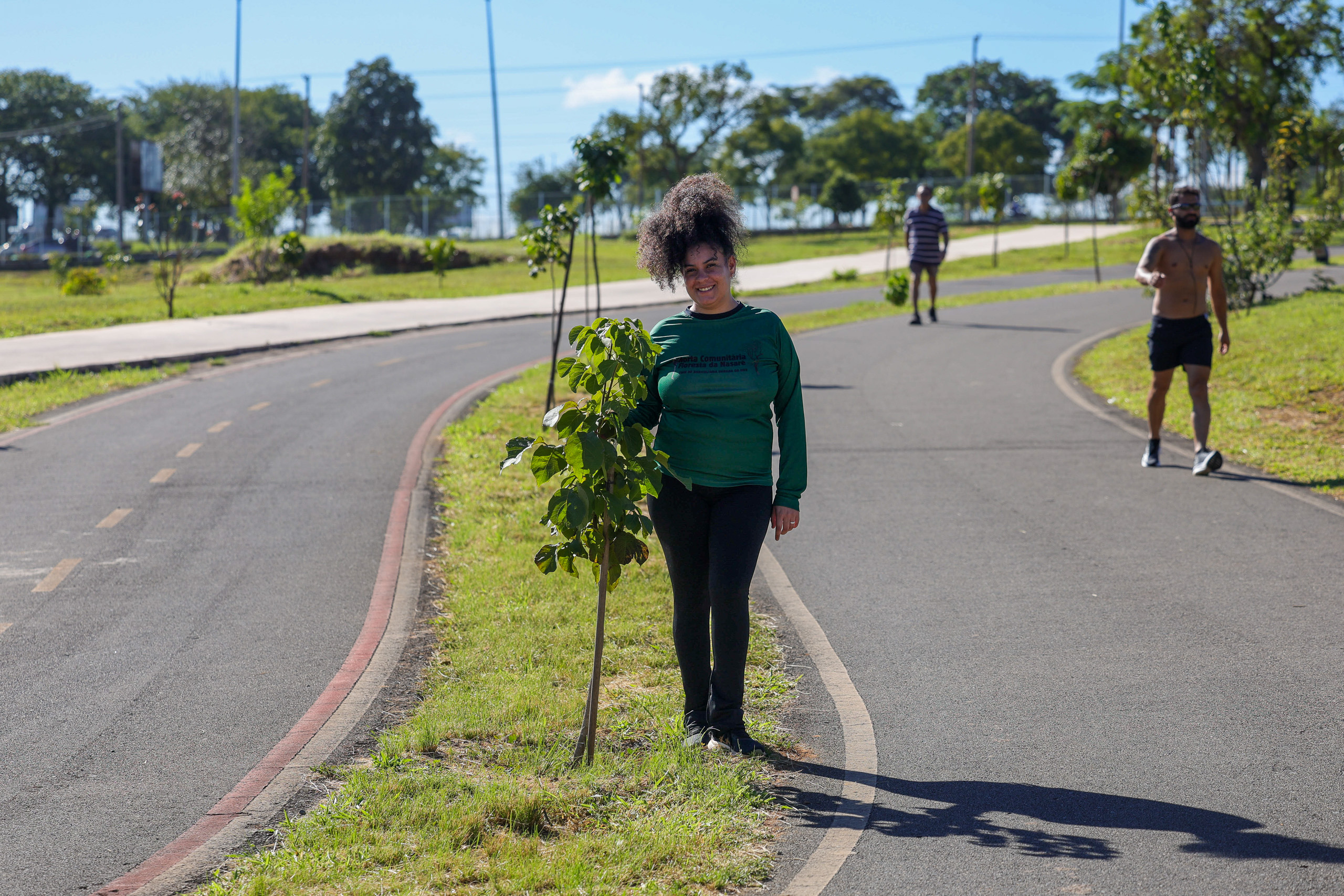 Woman with curly hair standing next to a tree on a bike path