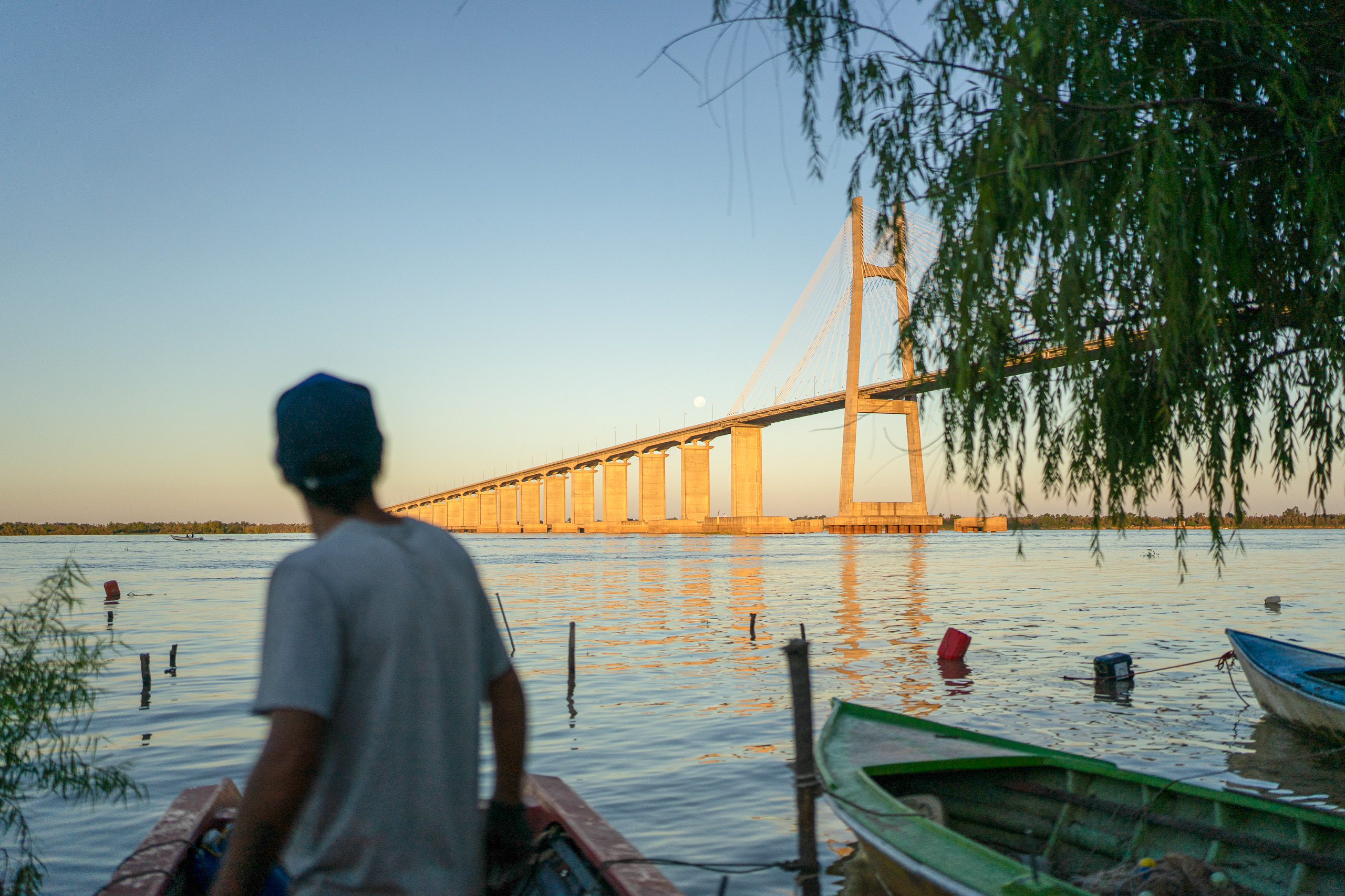 Un hombre de pie en un barco, contemplando un gran puente sobre el agua