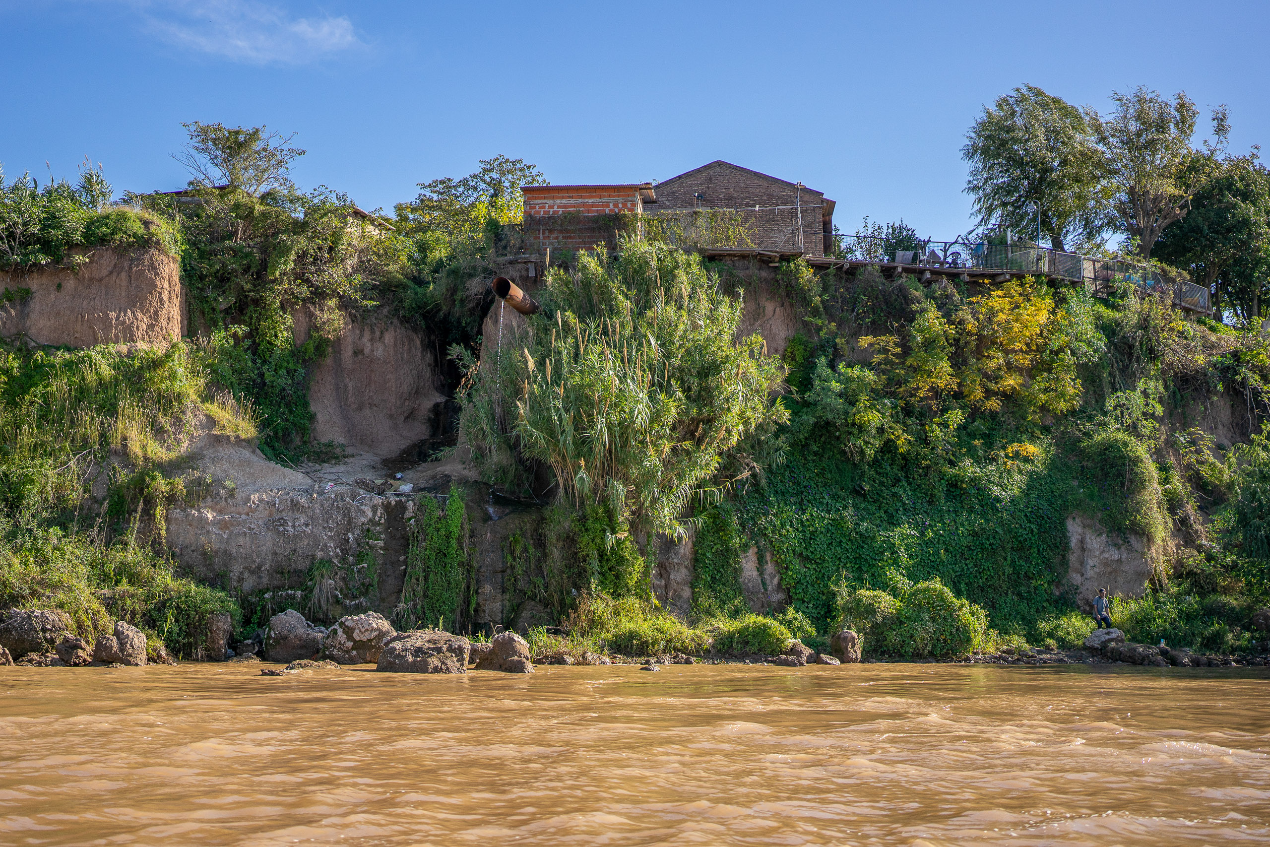 Río que discurre por un paisaje rocoso con una exuberante vegetación y edificios en lo alto