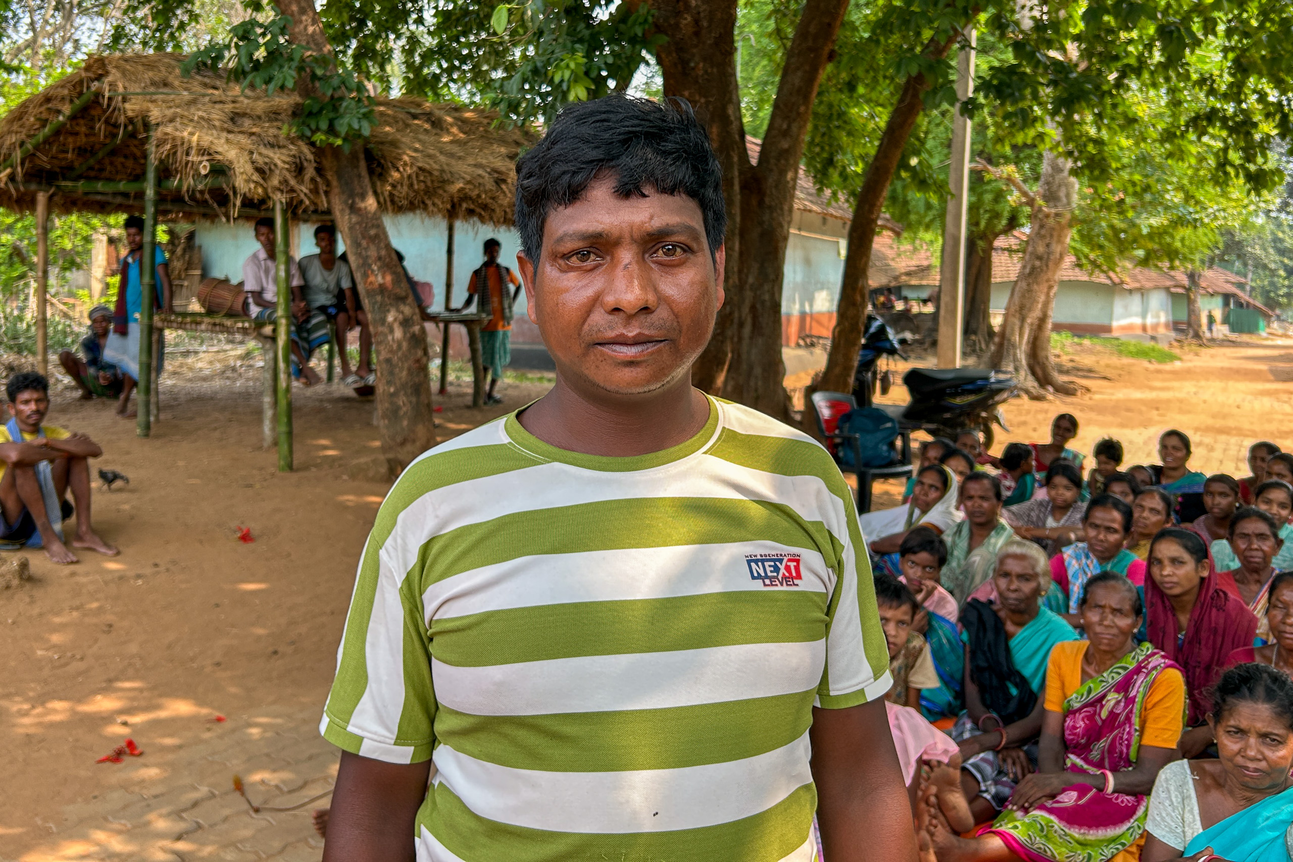 A man stands in front of a gathering of individuals in a rural village 