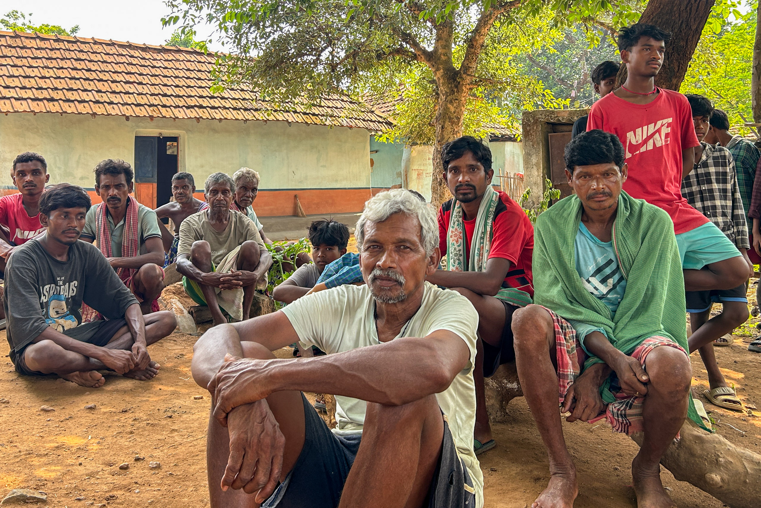 Men sitting on the ground gather for a meeting in a rural village