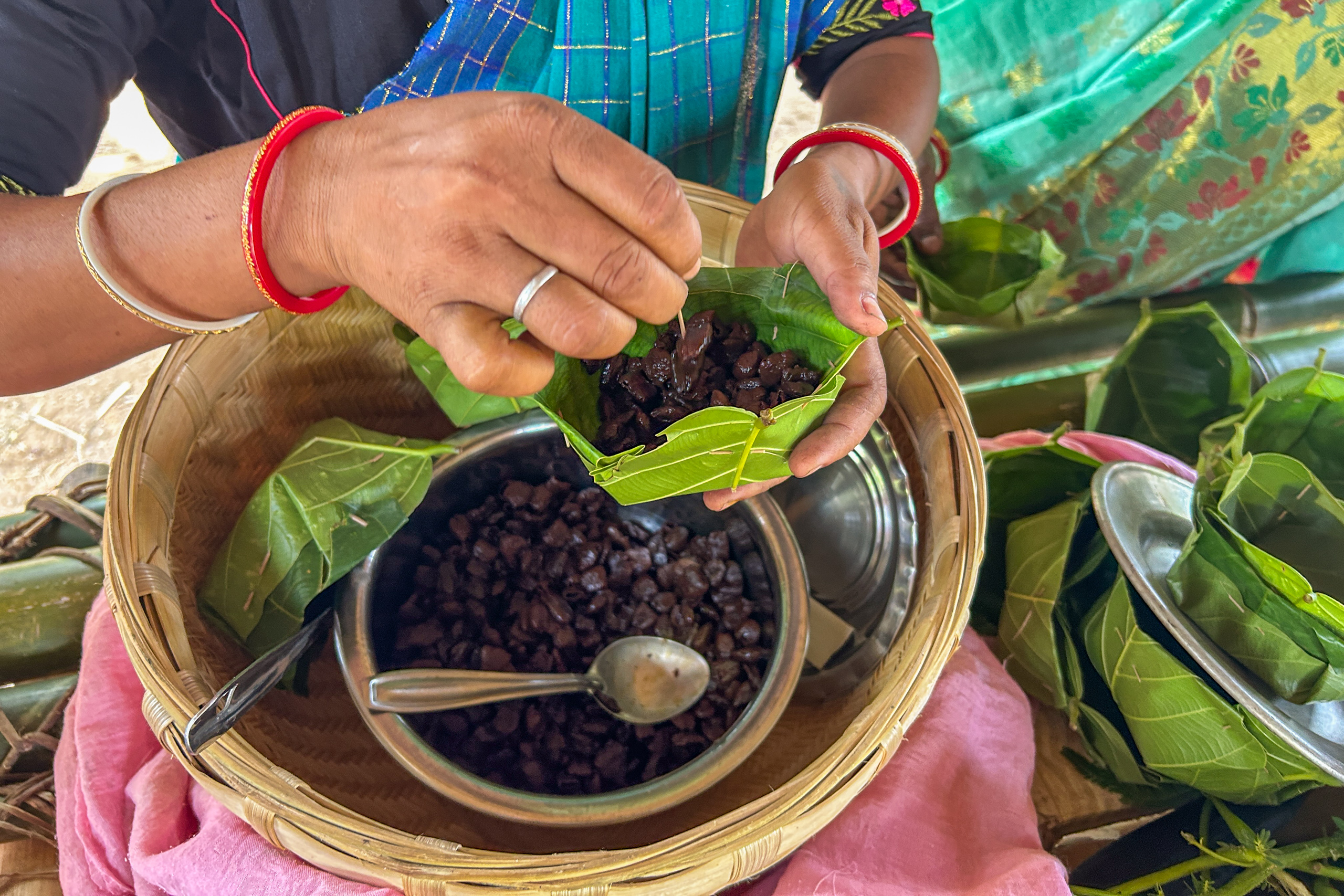 A hand holds a green leaf filled with dark food items