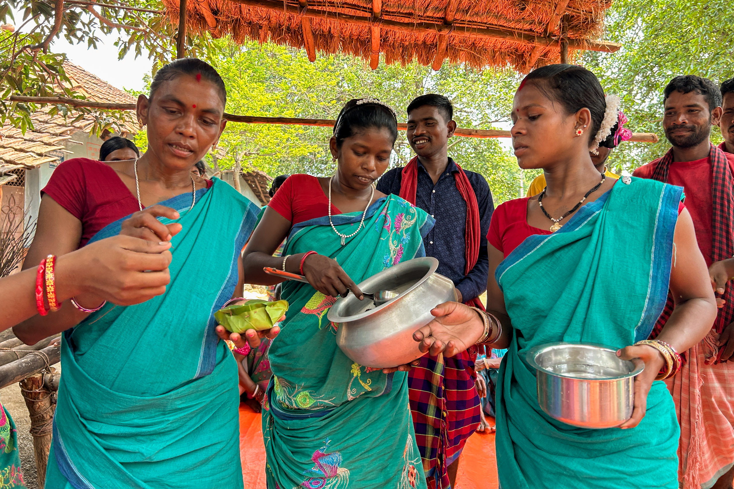 Women in green and blue traditional saris serve food under a shelter