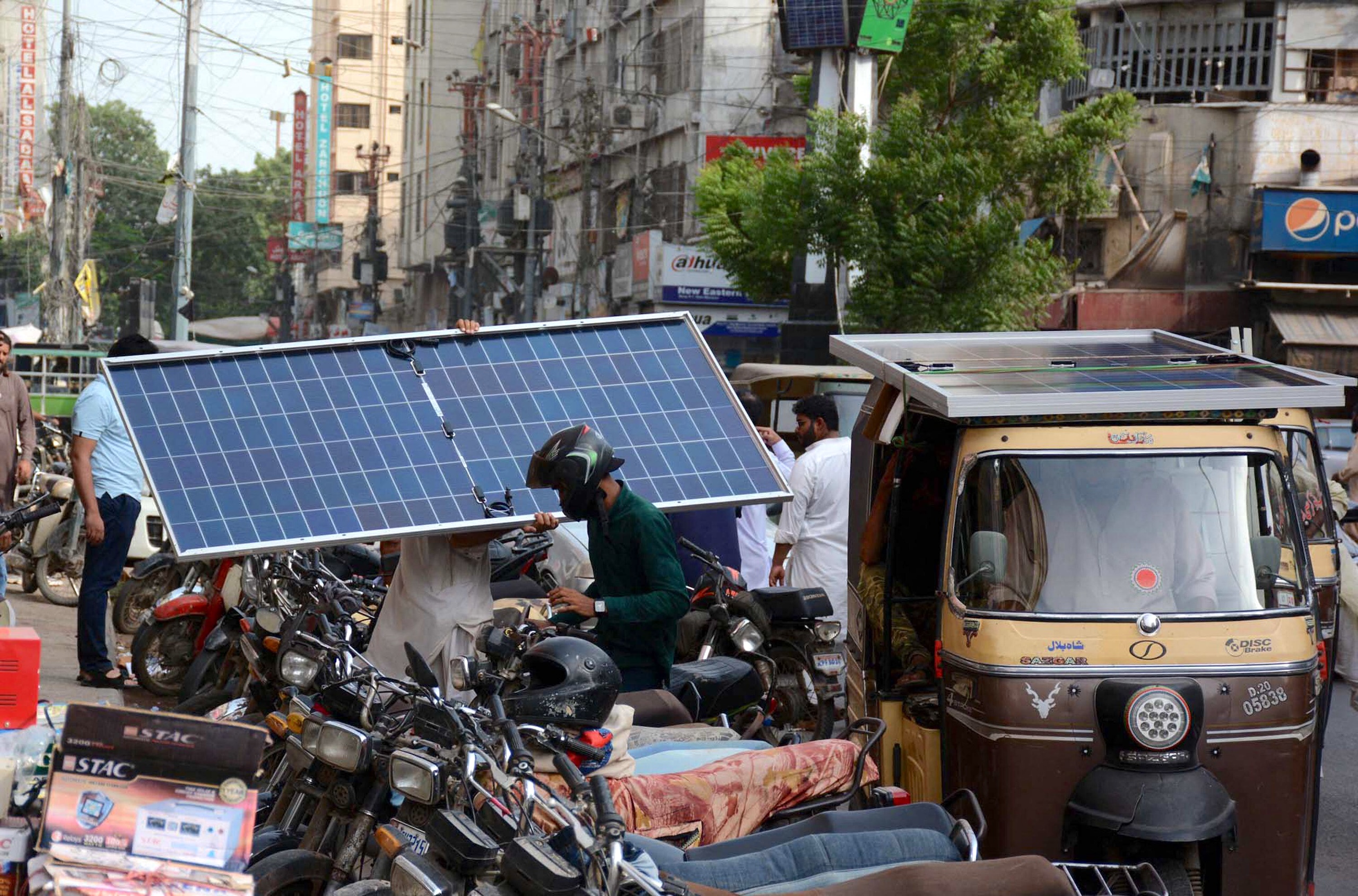 A man carries a solar panel walking in a busy street