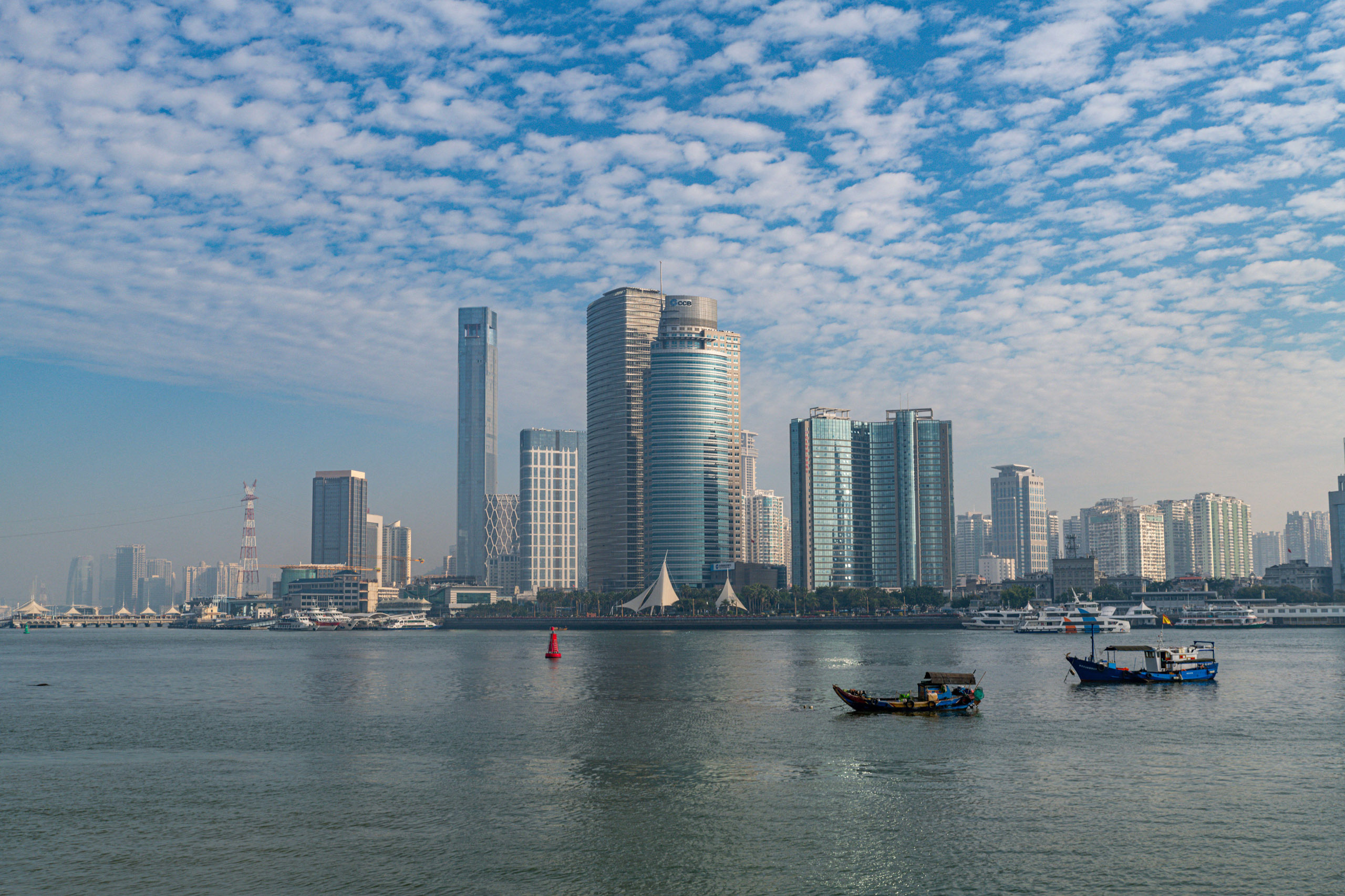 A waterfront scene with boats on water, a skyline of modern skyscrapers in the background