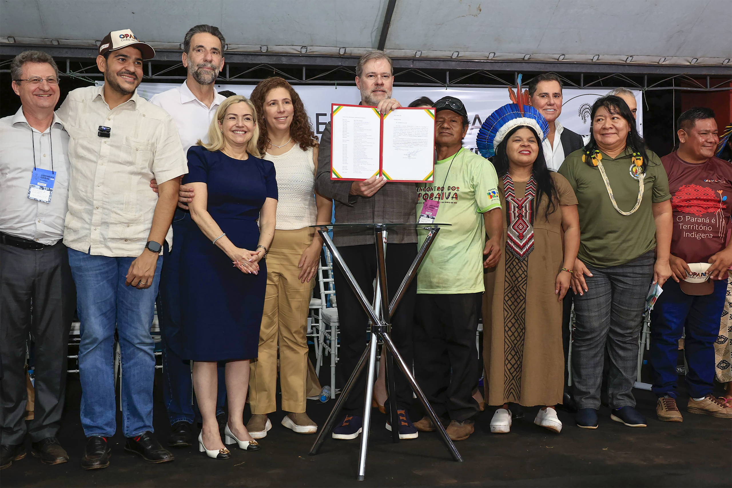 A diverse group of individuals gather on the stage with the man in the middle holding a piece of document in his hands
