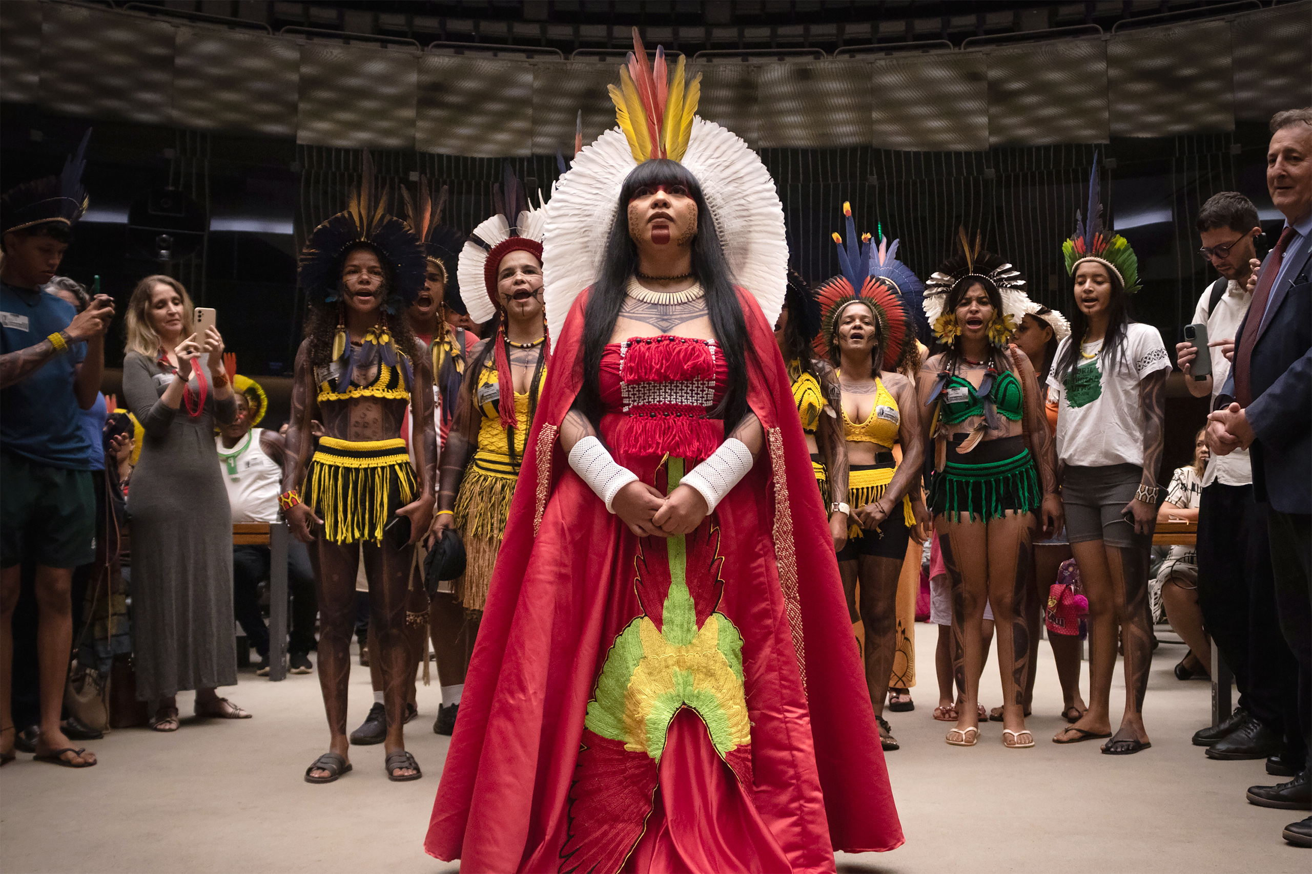 group of indiginous people in regalia led by woman in red