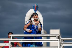 Indigenous woman in blue speaking into microphone