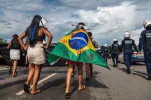 indigenous people with Brazil flag walking in street near line of police officers