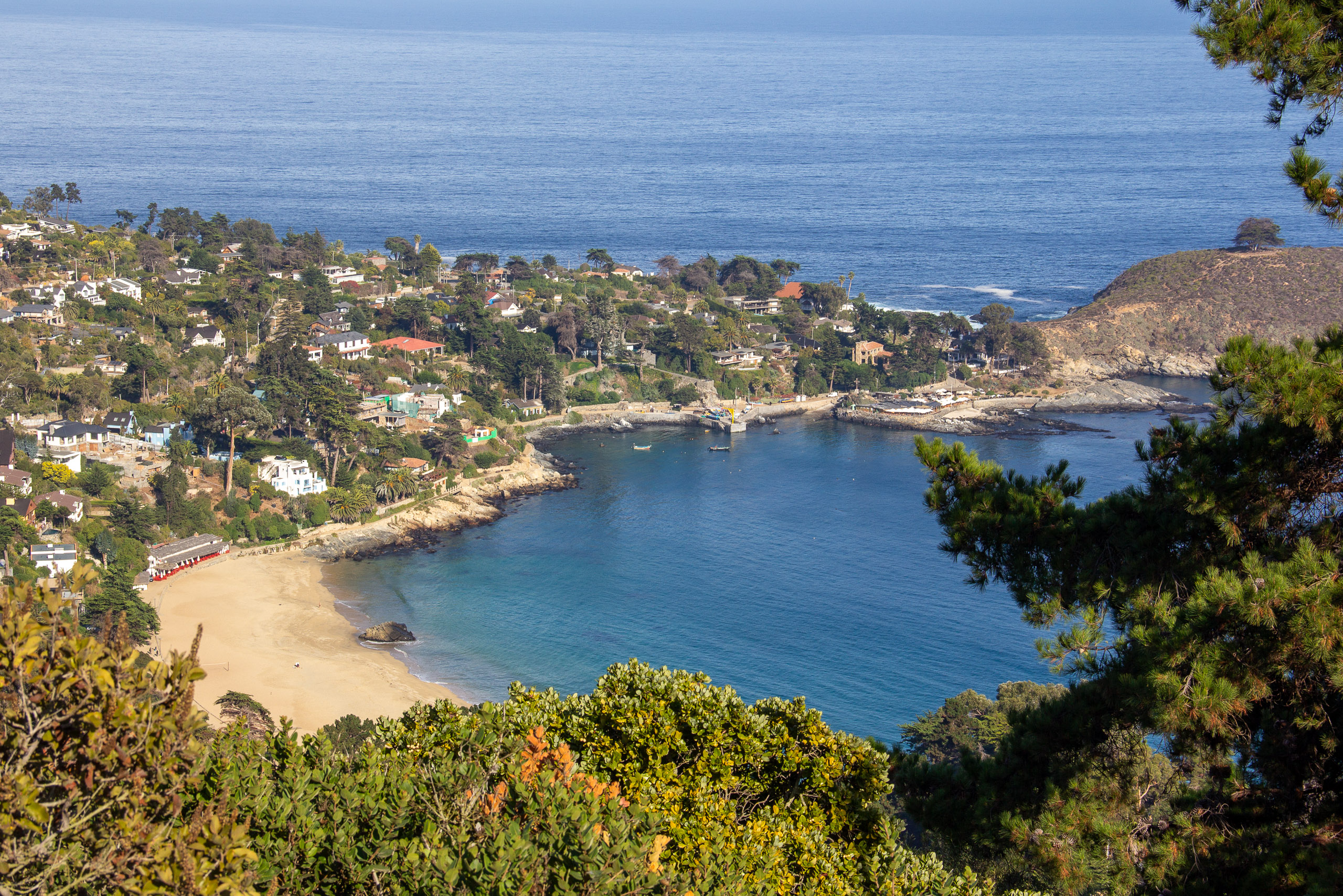 A high-angle view of a coastal town on a hillside overlooking a beach and blue bay.